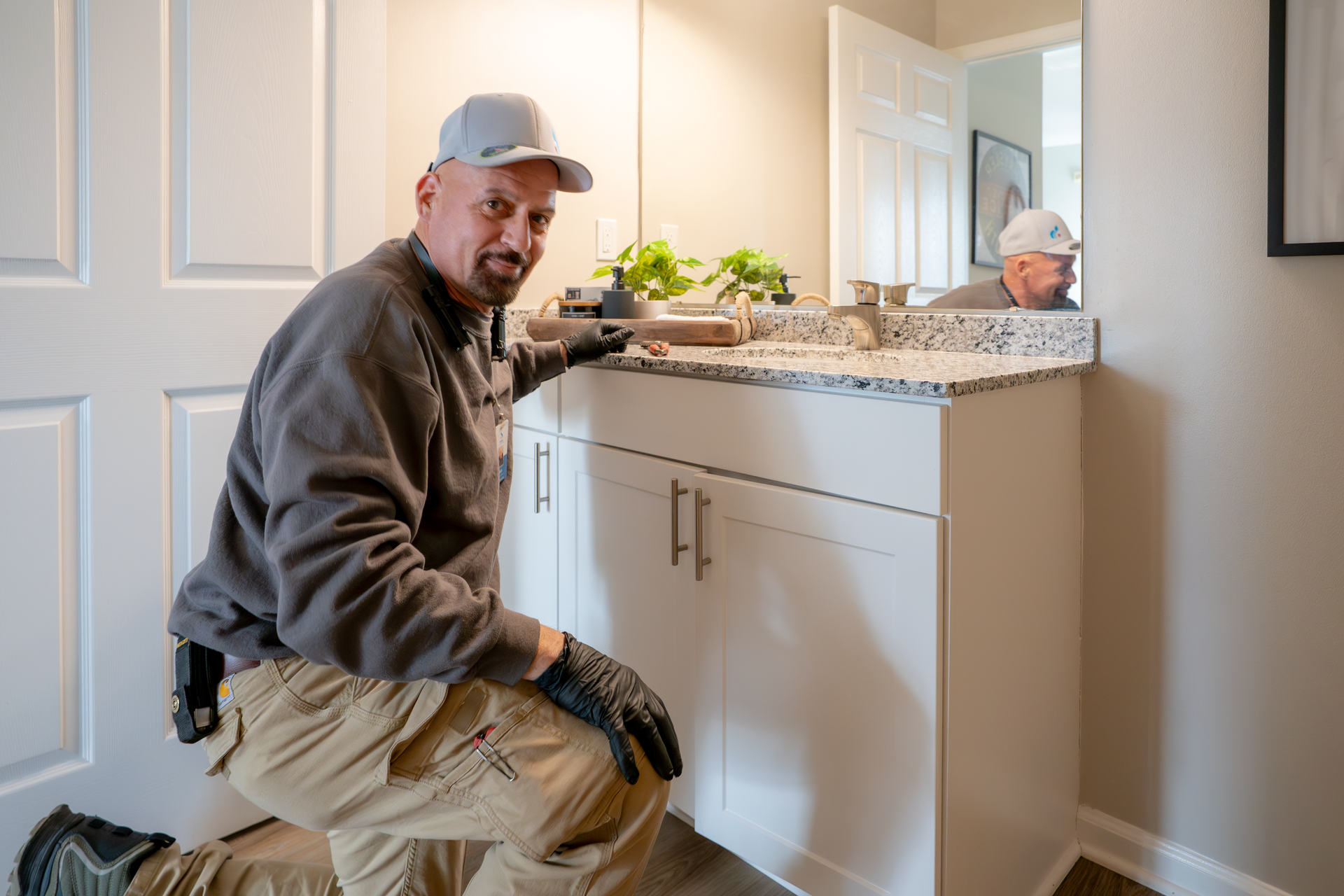 Worker installing a bathroom vanity with granite countertop in a bright hallway bathroom