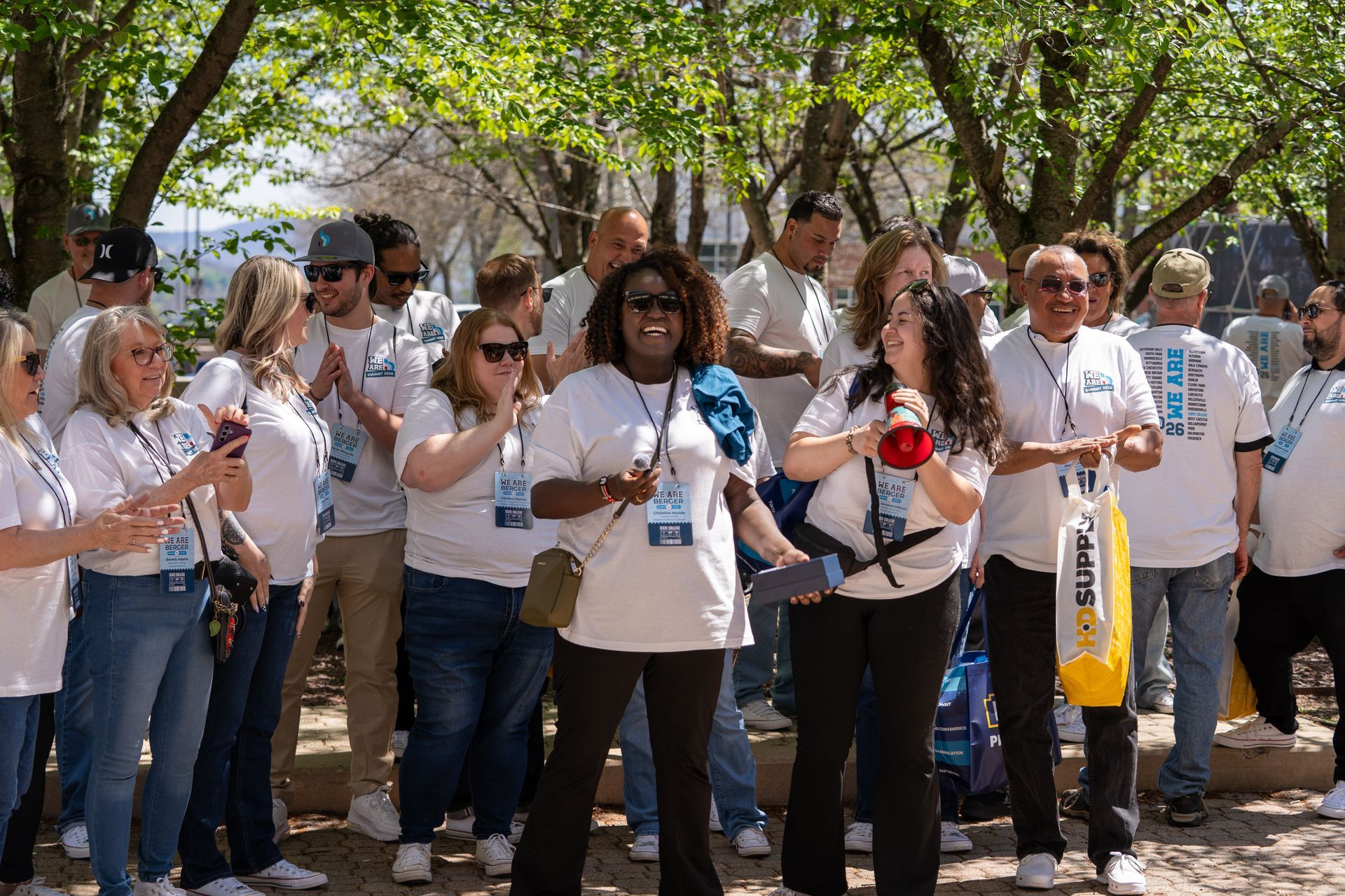Crowd of people in white shirts standing outdoors, holding flowers and signs at a gathering