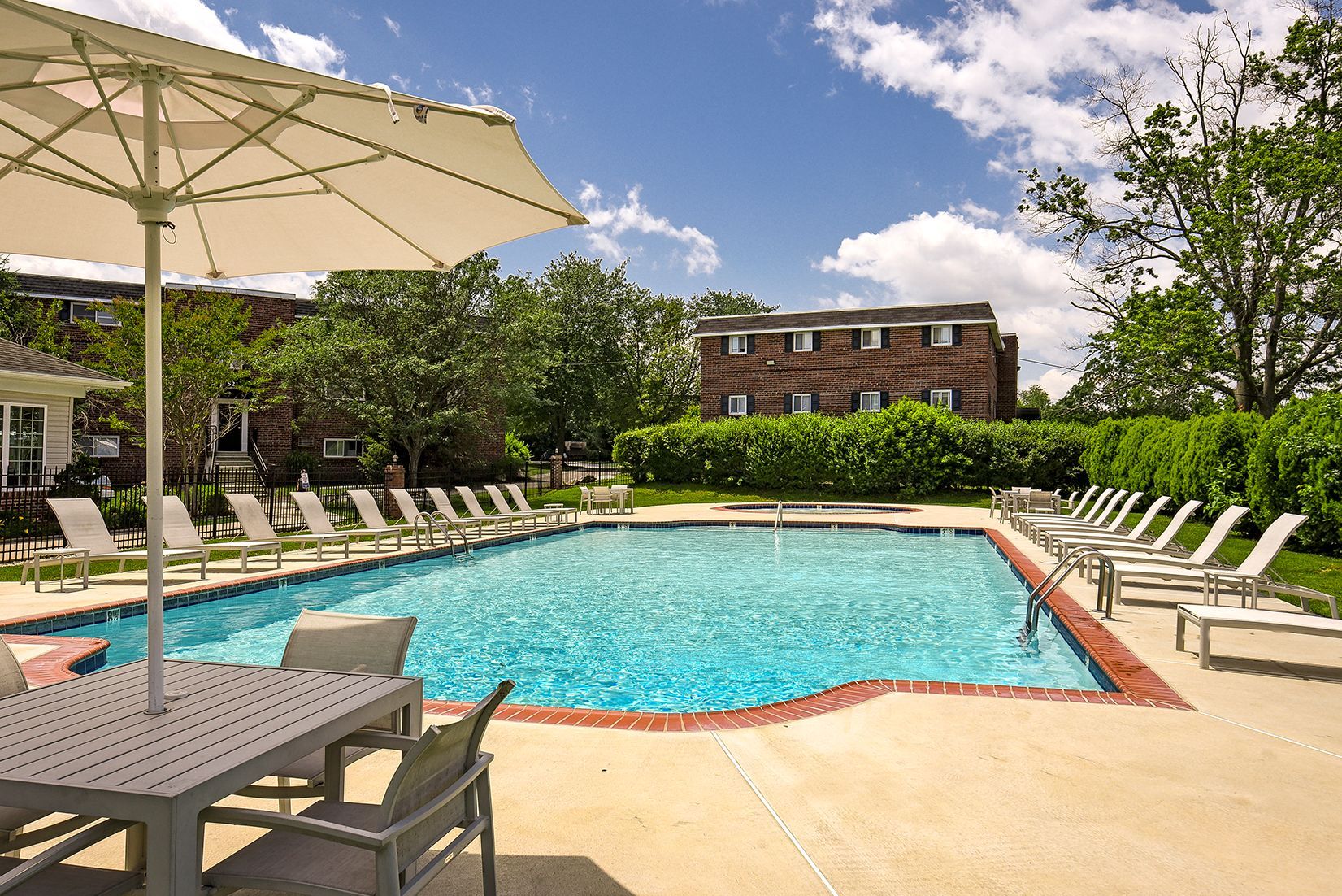 Outdoor swimming pool with lounge chairs, umbrellas, and trees on a sunny day