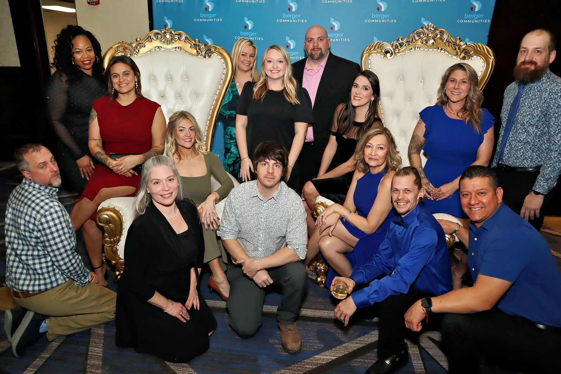 Group posing on ornate gold chairs at an awards-style event backdrop
