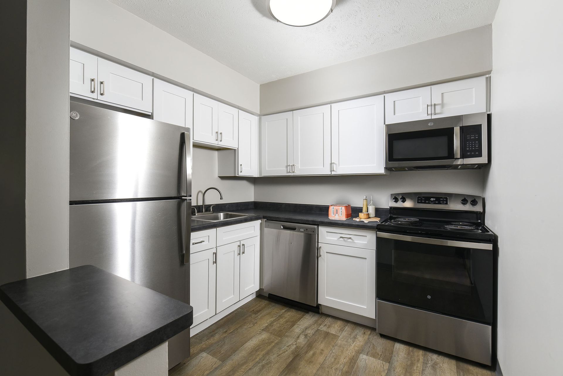 Modern kitchen with stainless steel appliances, white cabinets, black countertops, and a small table