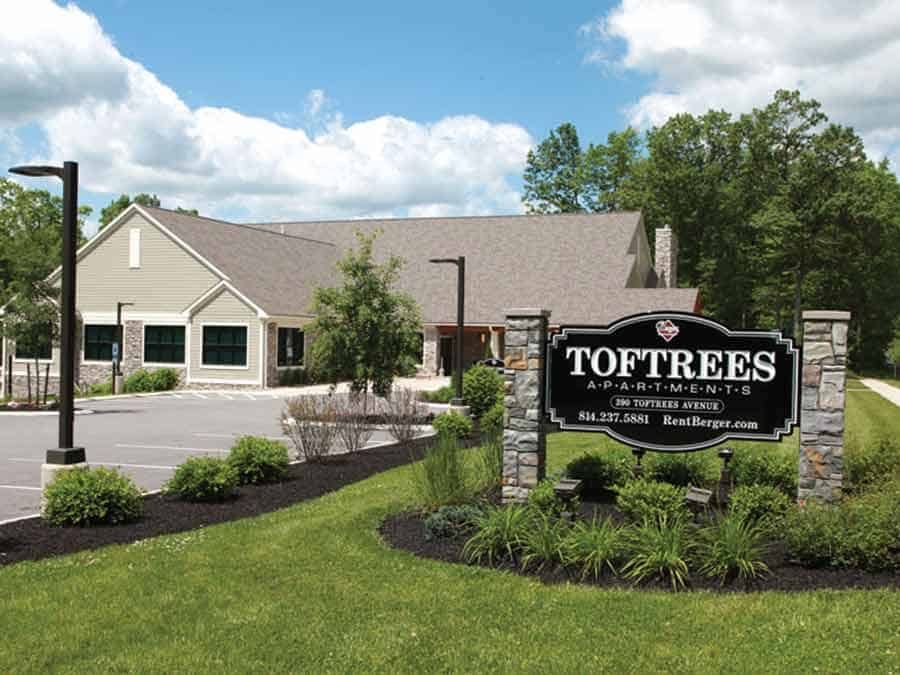 Sign for Toftrees Apartments in front of a tan building and landscaping on a sunny day.