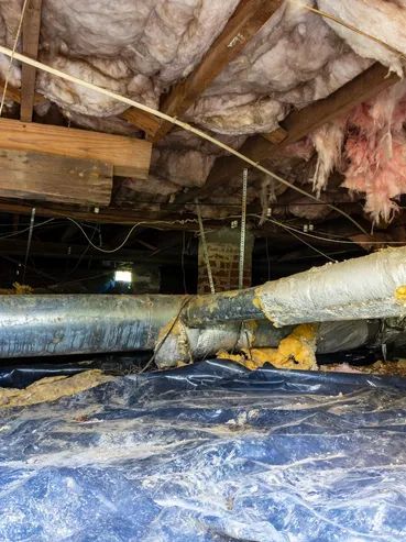 Crawl space with insulation, ductwork, and vapor barrier. Wooden beams, brick chimney.