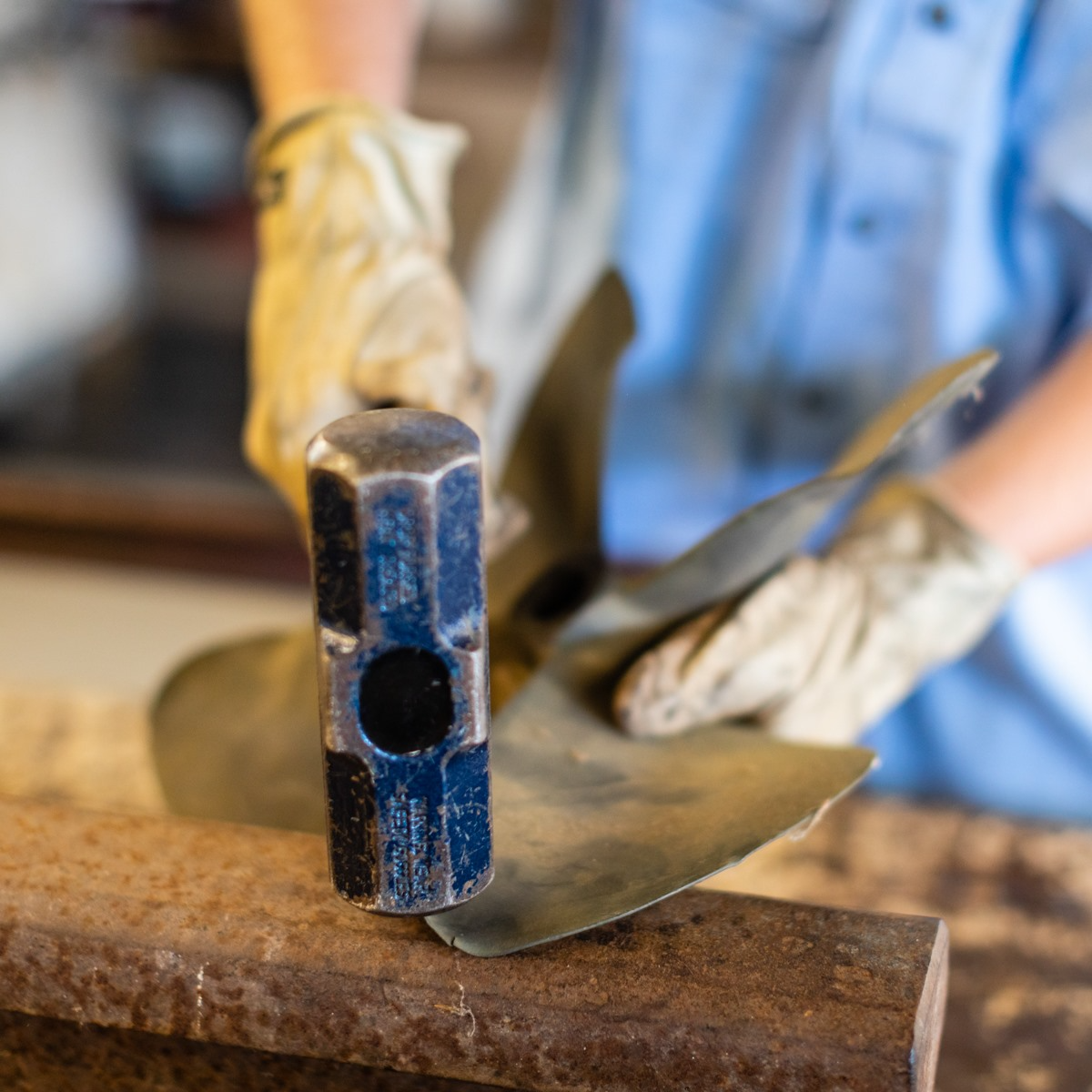 A person in work gloves uses a hammer on metal, working on a project.