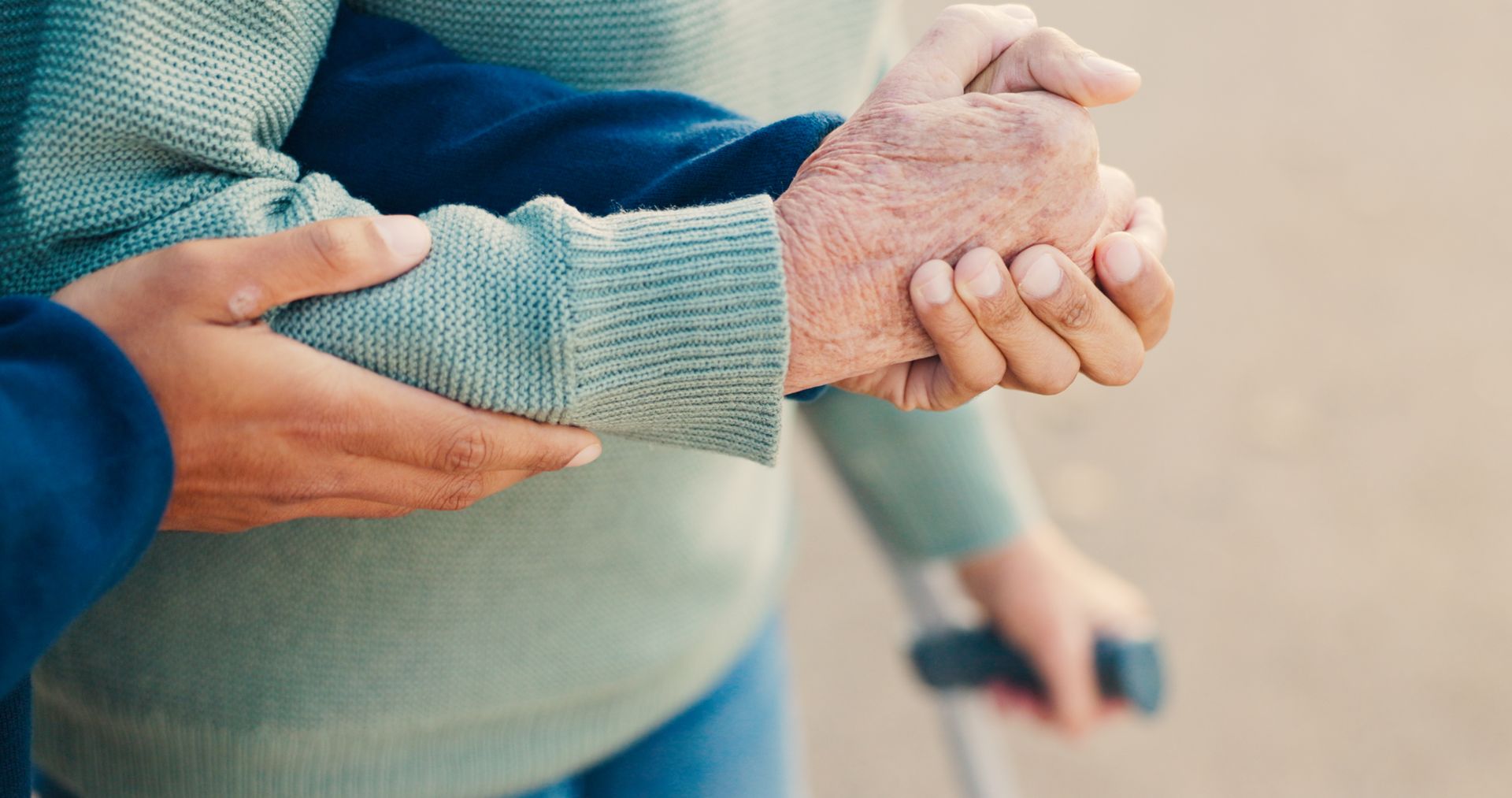 Caregiver holding the hand of an elderly person with a cane for senior home care help.
