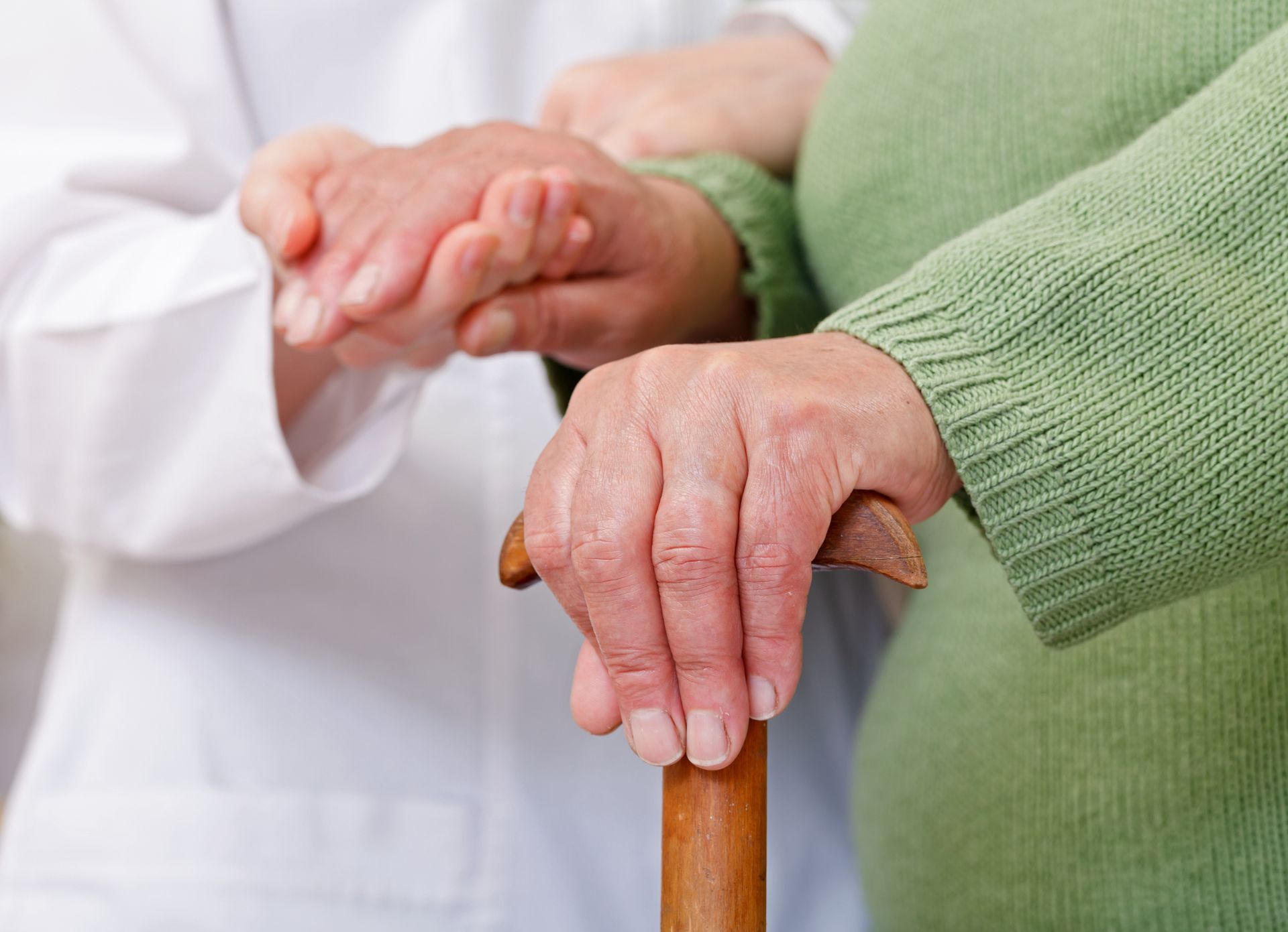 aregiver assisting an elderly person with a wooden cane; professional senior home care.