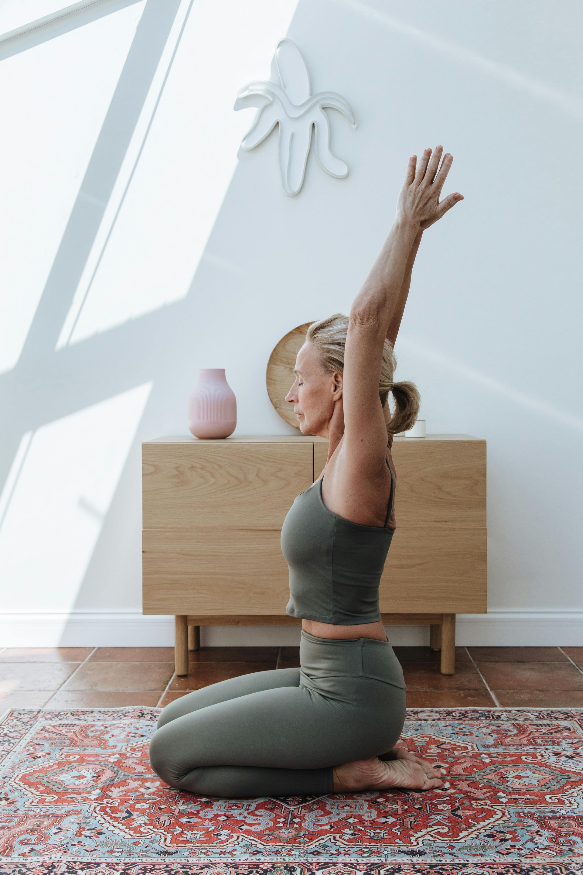 A woman is kneeling on the floor doing yoga in a living room.