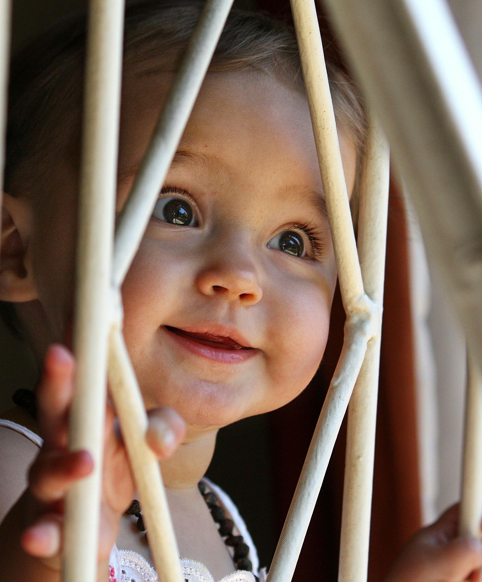 A little girl is looking through a fence and smiling