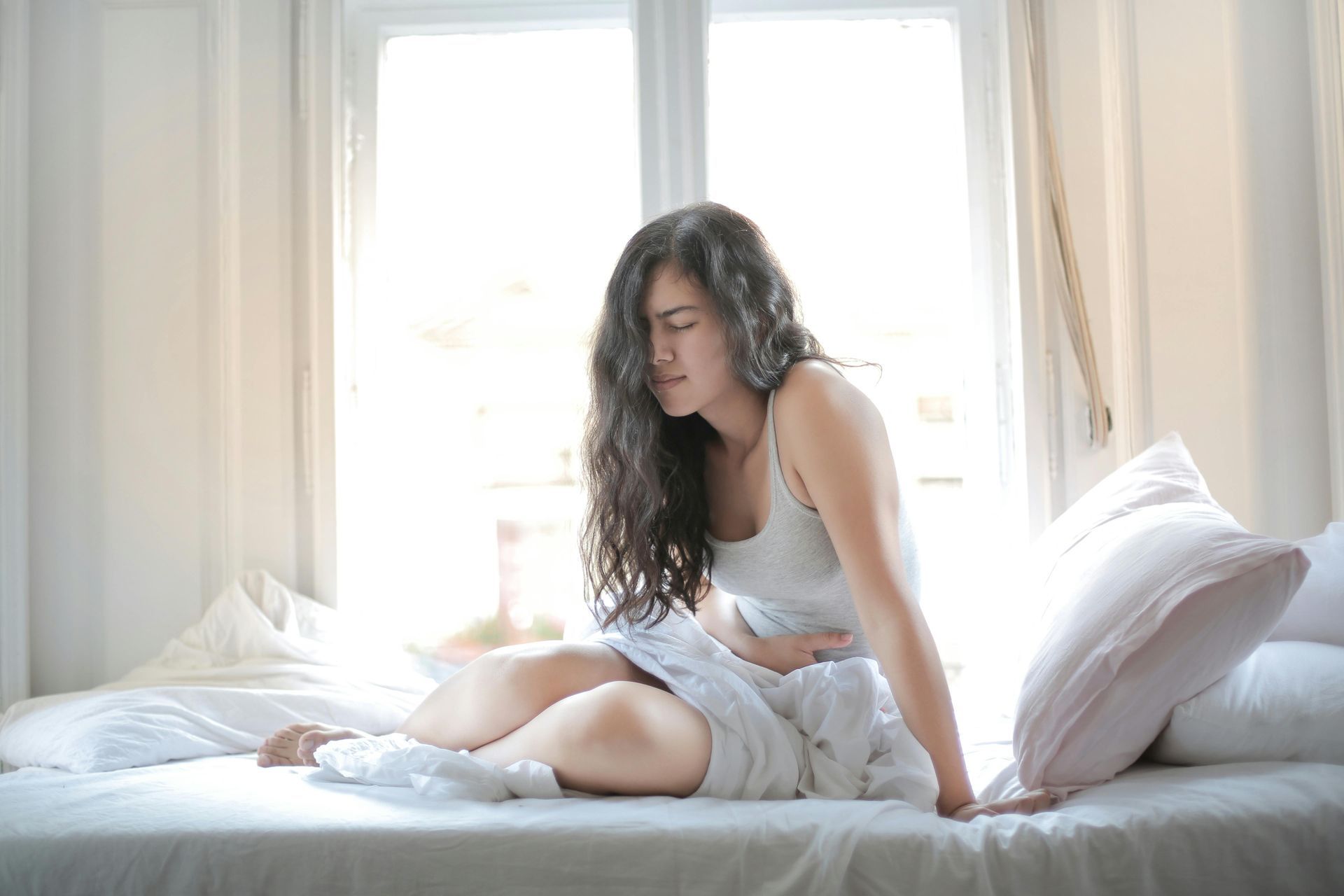 A woman is sitting on a bed holding her stomach.