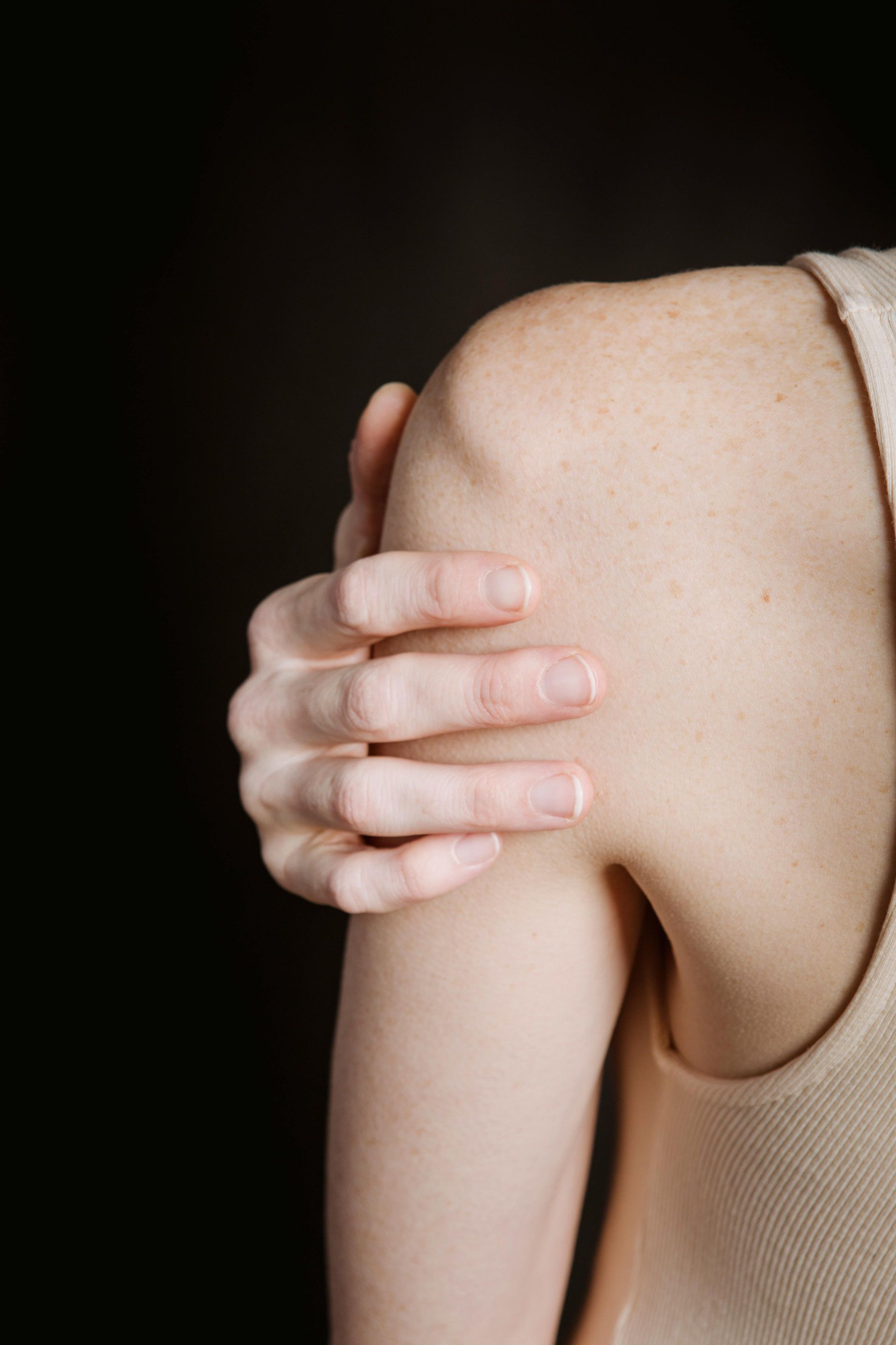 A woman is holding her shoulder in pain.