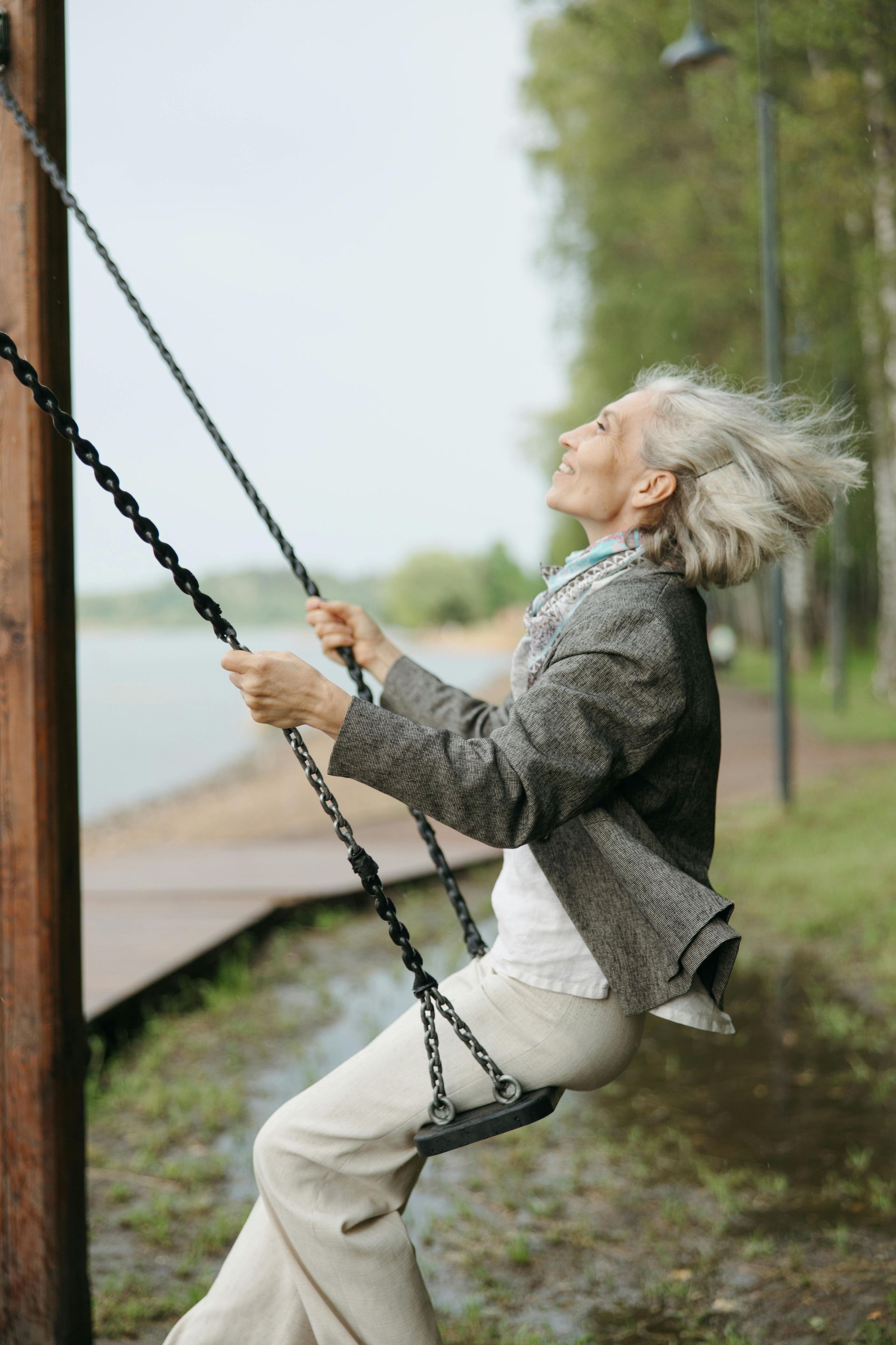 An elderly woman is sitting on a swing in a park.