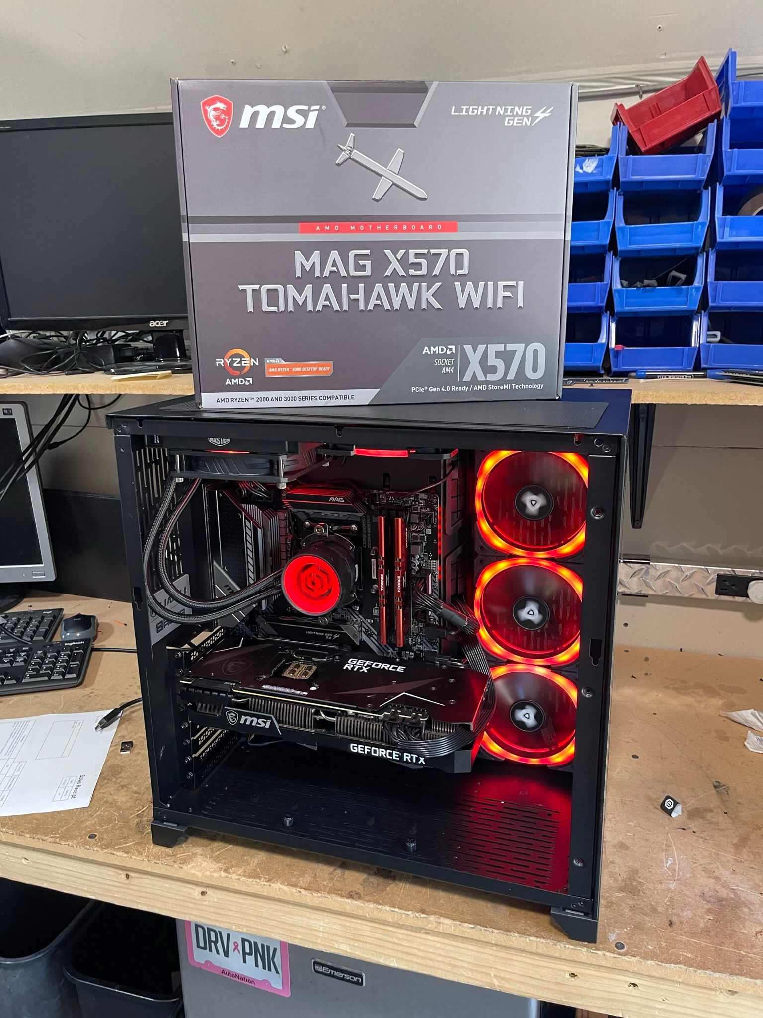 Open PC case with RGB-lit cooling fans beside an MSI MAG X570 TOMAHAWK WIFI motherboard box.