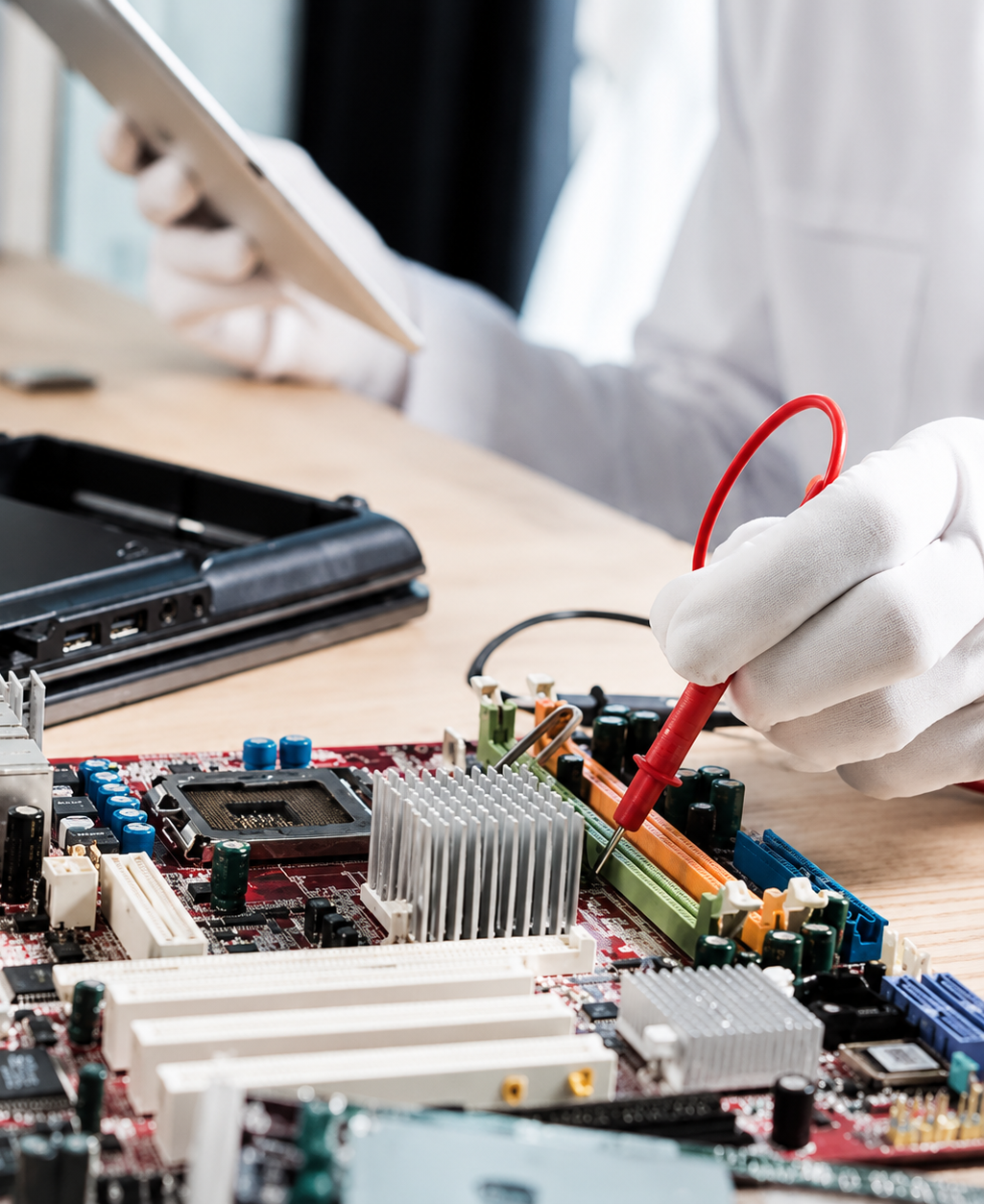 Gloved technician probing a computer motherboard with a red multimeter lead at a workbench