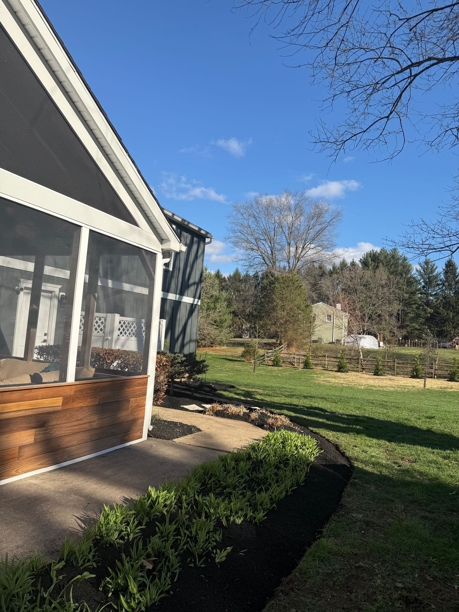 Back porch and screened patio beside a grassy yard under a clear blue sky