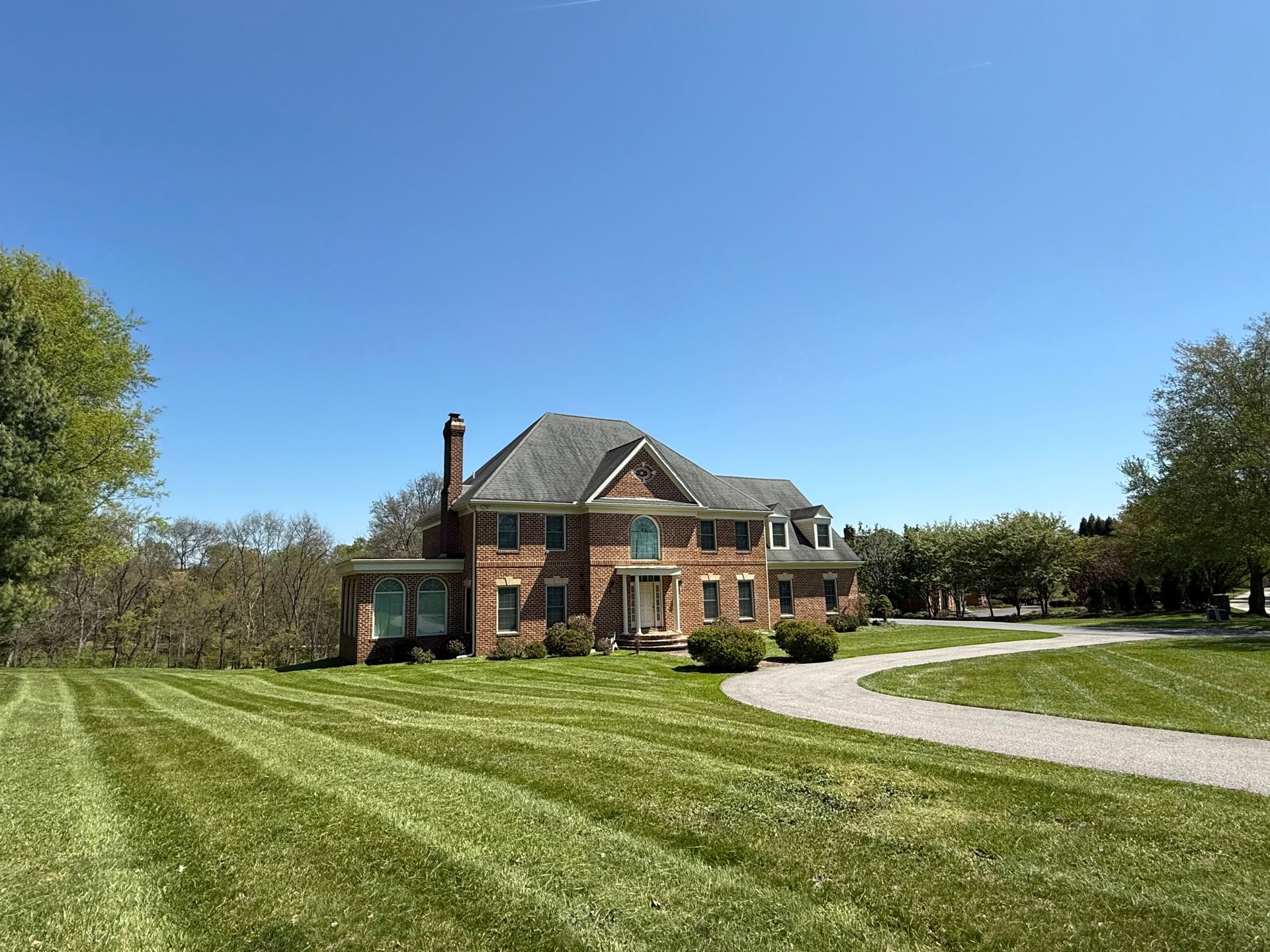 Brick house with green lawn and curving driveway under a clear blue sky