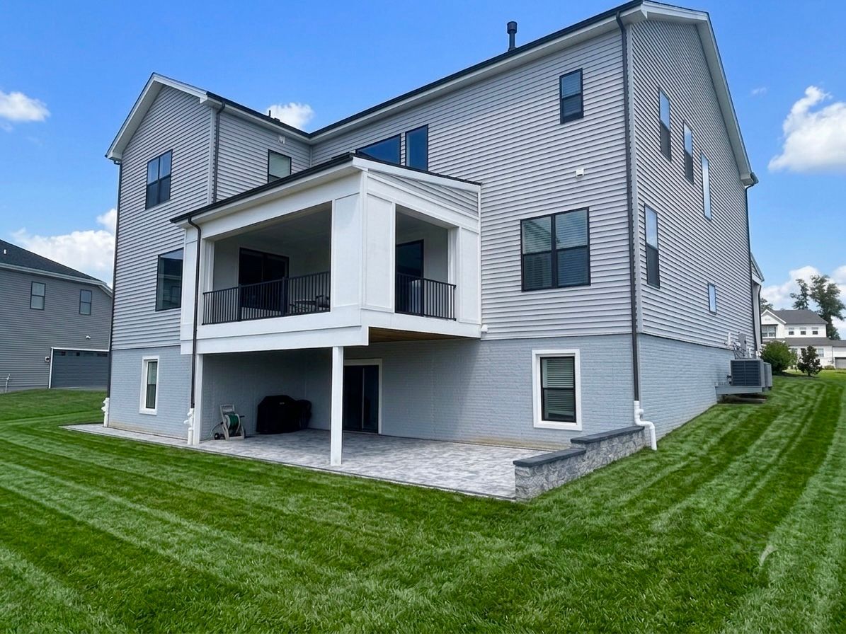 Gray two-story house with a covered back porch and green lawn under a blue sky