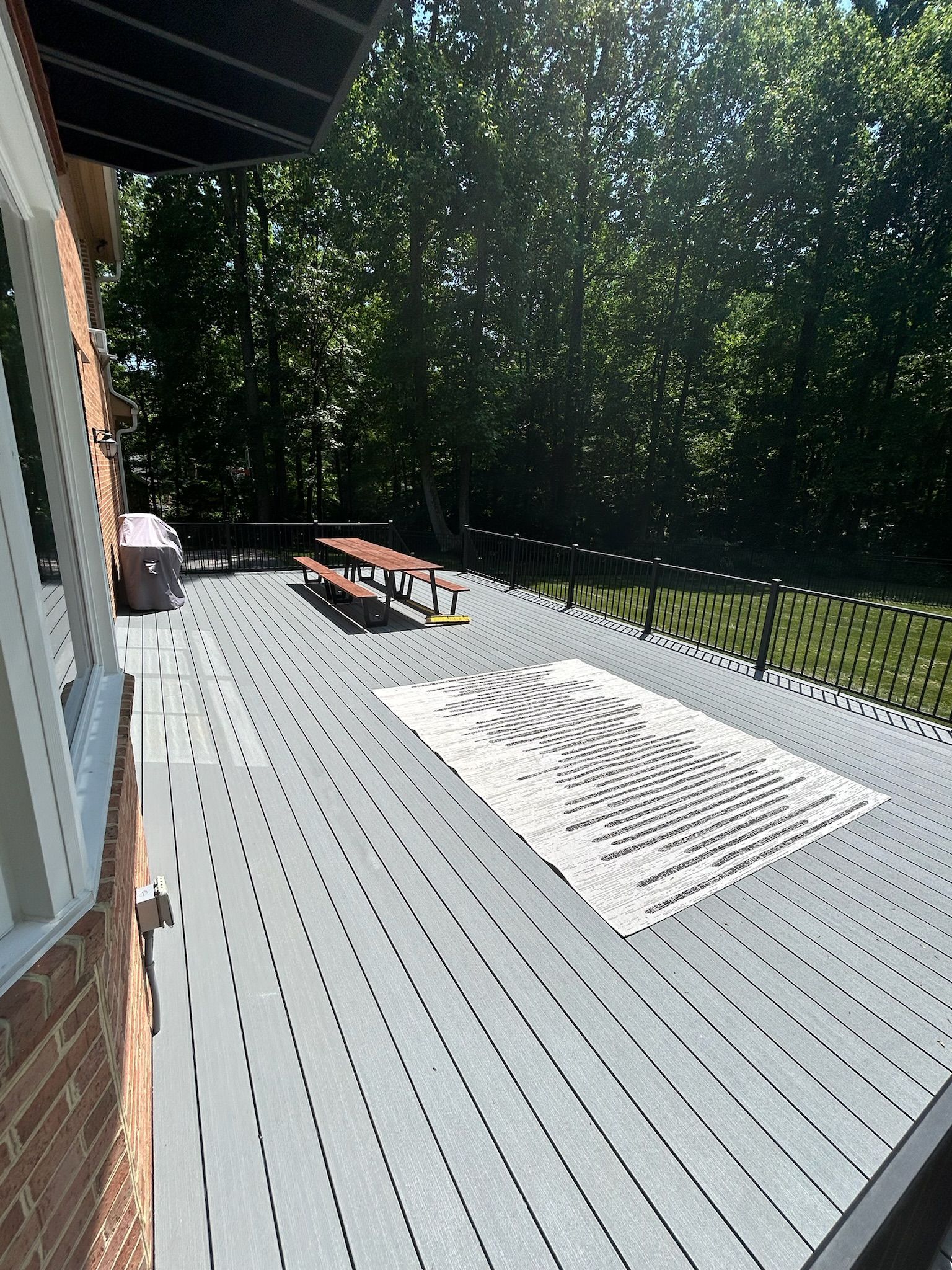 Wooden deck with lounge chairs and a bright rug beside a house, surrounded by trees in sunlight