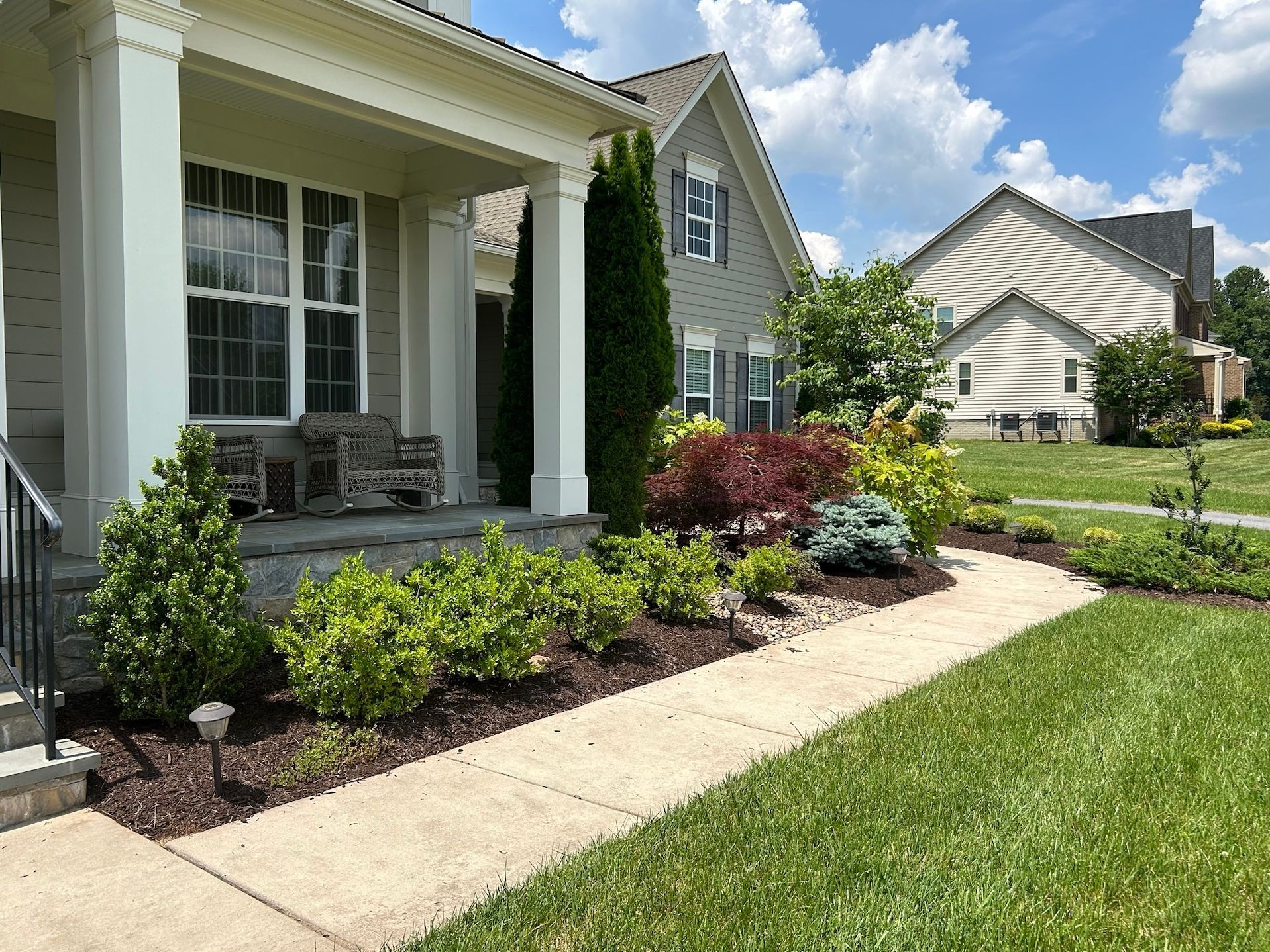 Suburban house front porch with columns, landscaped flower beds, and a concrete walkway