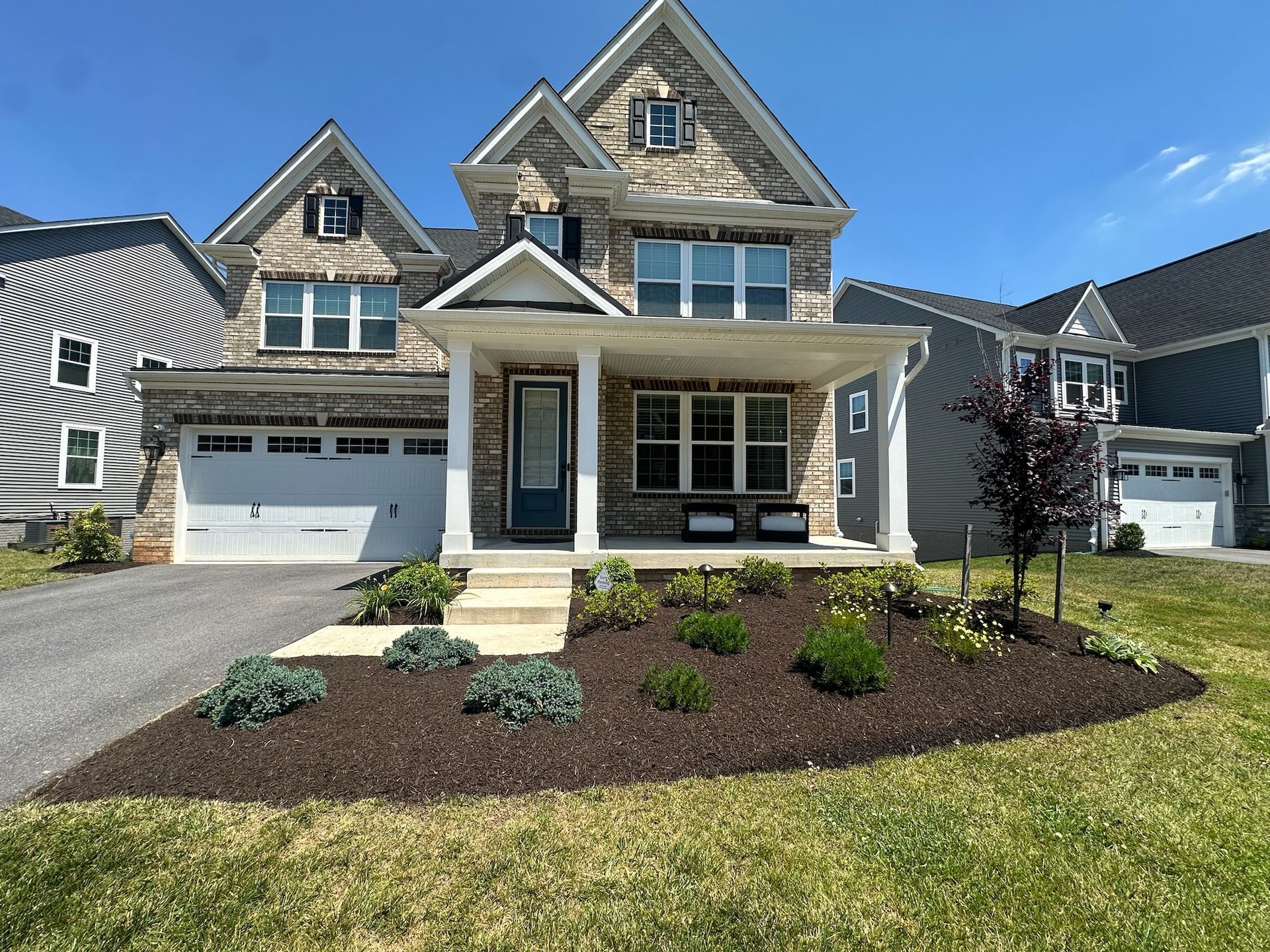 New suburban house with stone facade, front porch, double garage, and landscaped front yard under a blue sky
