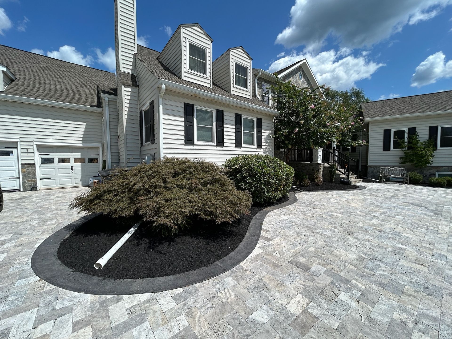 Charming white house with black shutters, dormers, and stone driveway under a bright blue sky