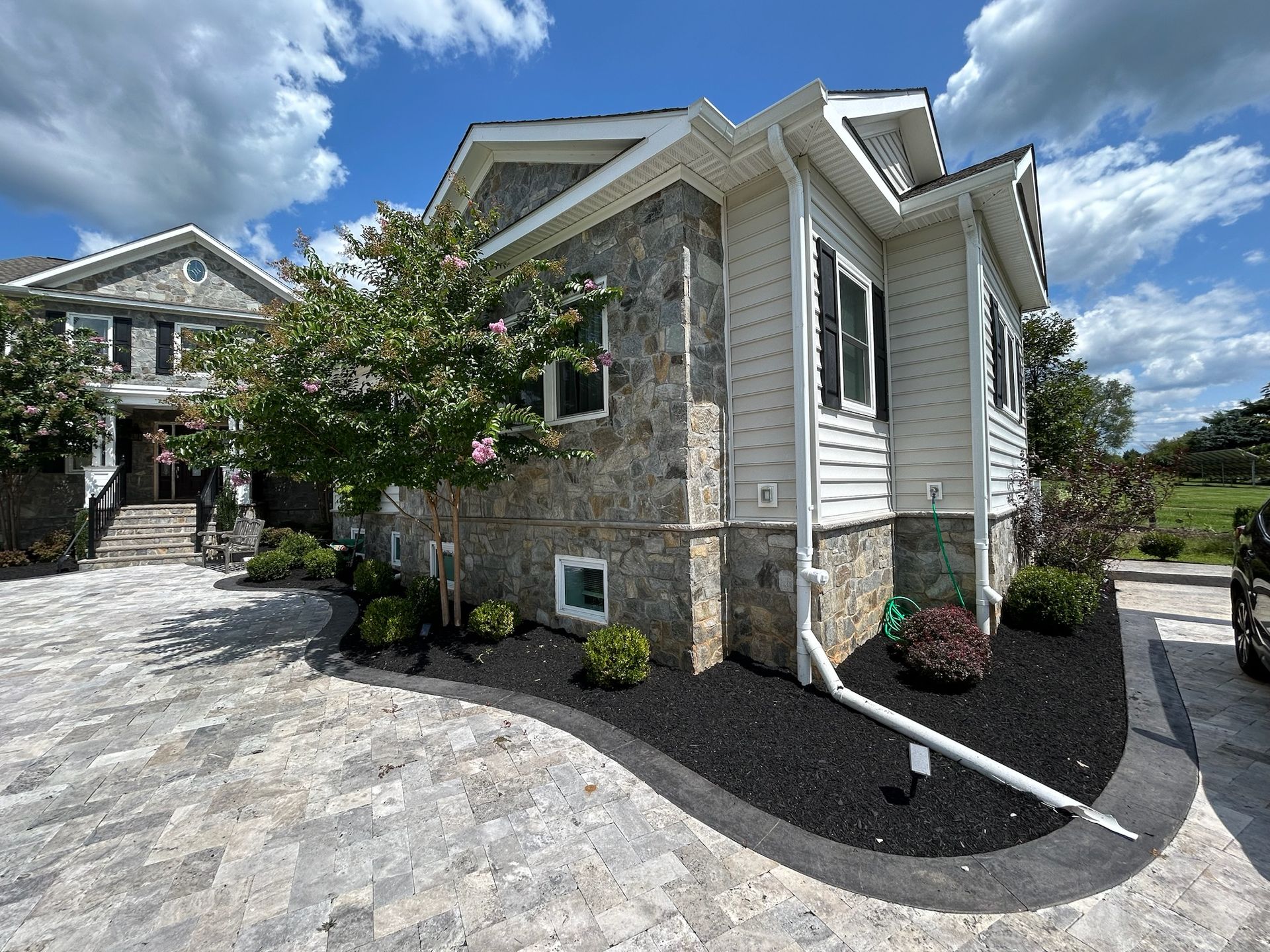 Stone house exterior with white trim, curved driveway, and landscaped front yard under a blue sky