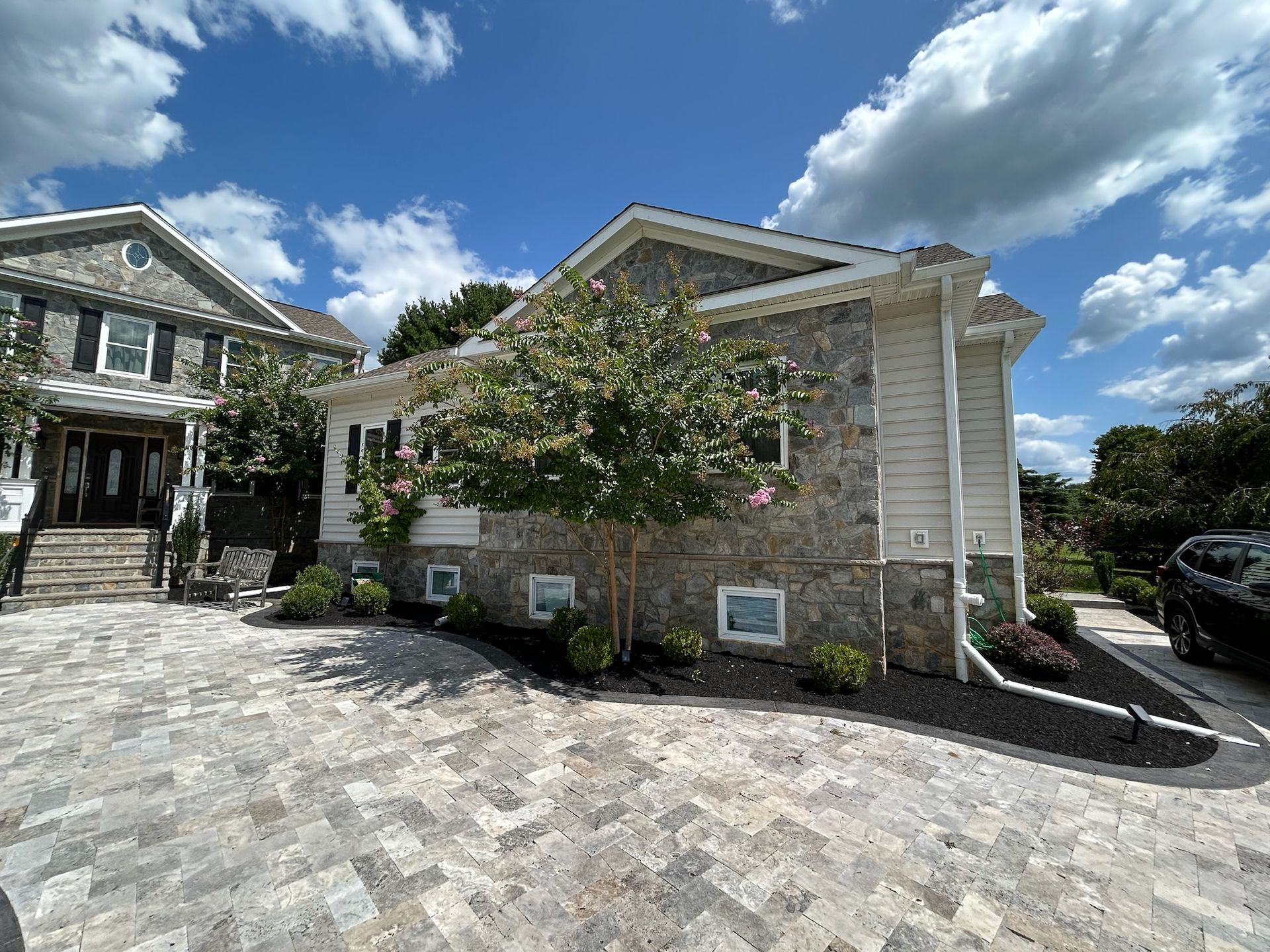 Suburban stone house with white trim, paved driveway, and blue sky with clouds