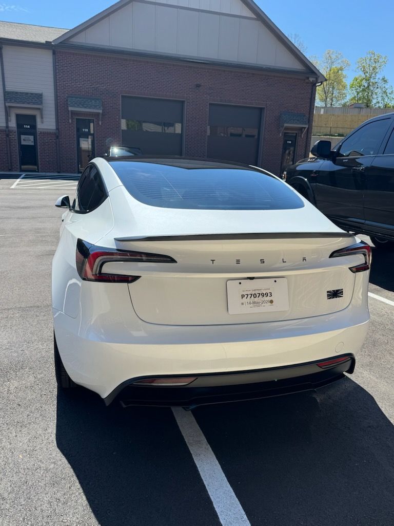 White Tesla sedan parked in a lot in front of a brick building, rear view.