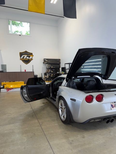 Silver sports car with rear hatch open and driver door ajar in a garage workshop
