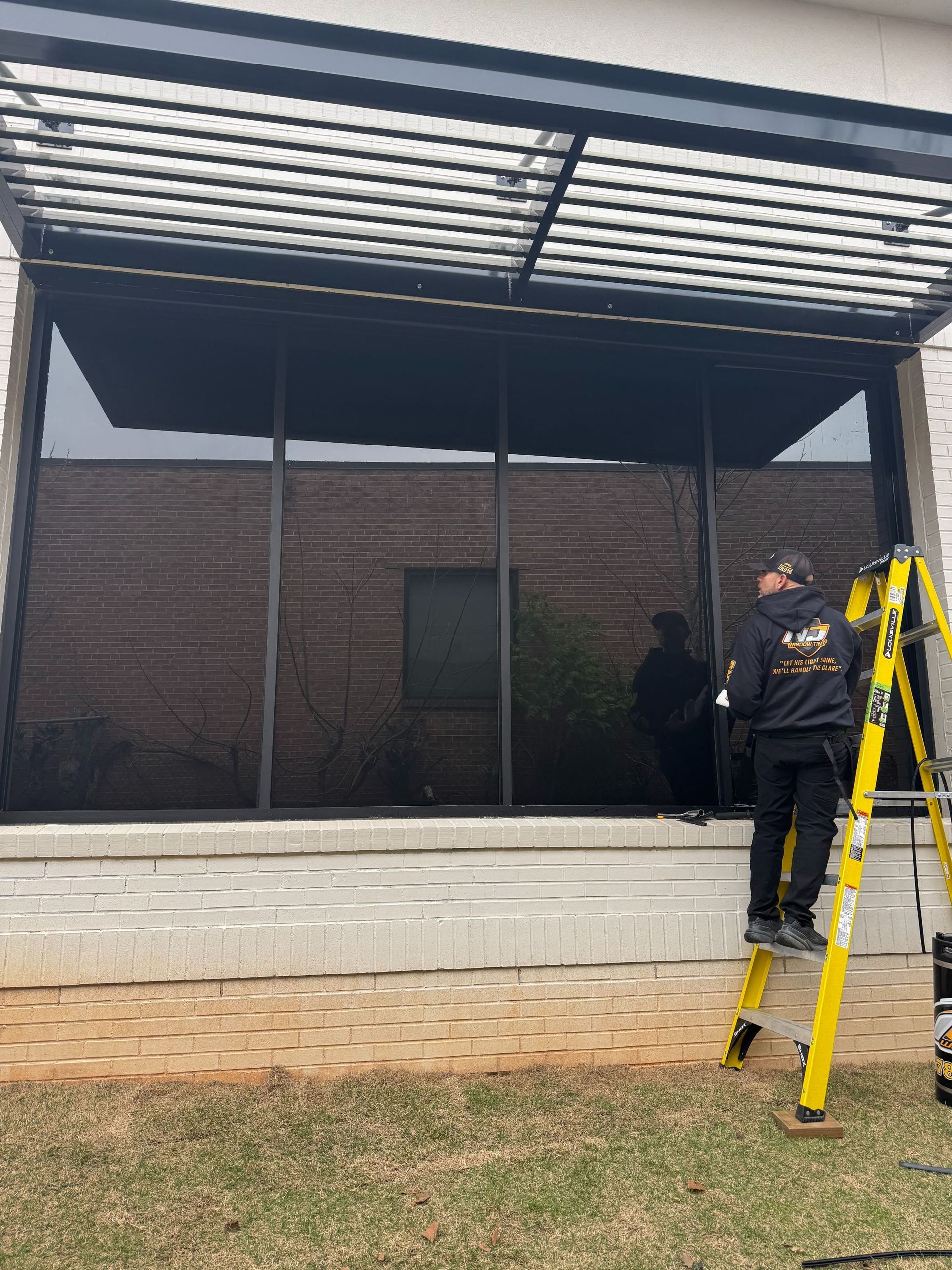 Yellow ladders beside a brick building with a covered patio; two workers stand near the wall.