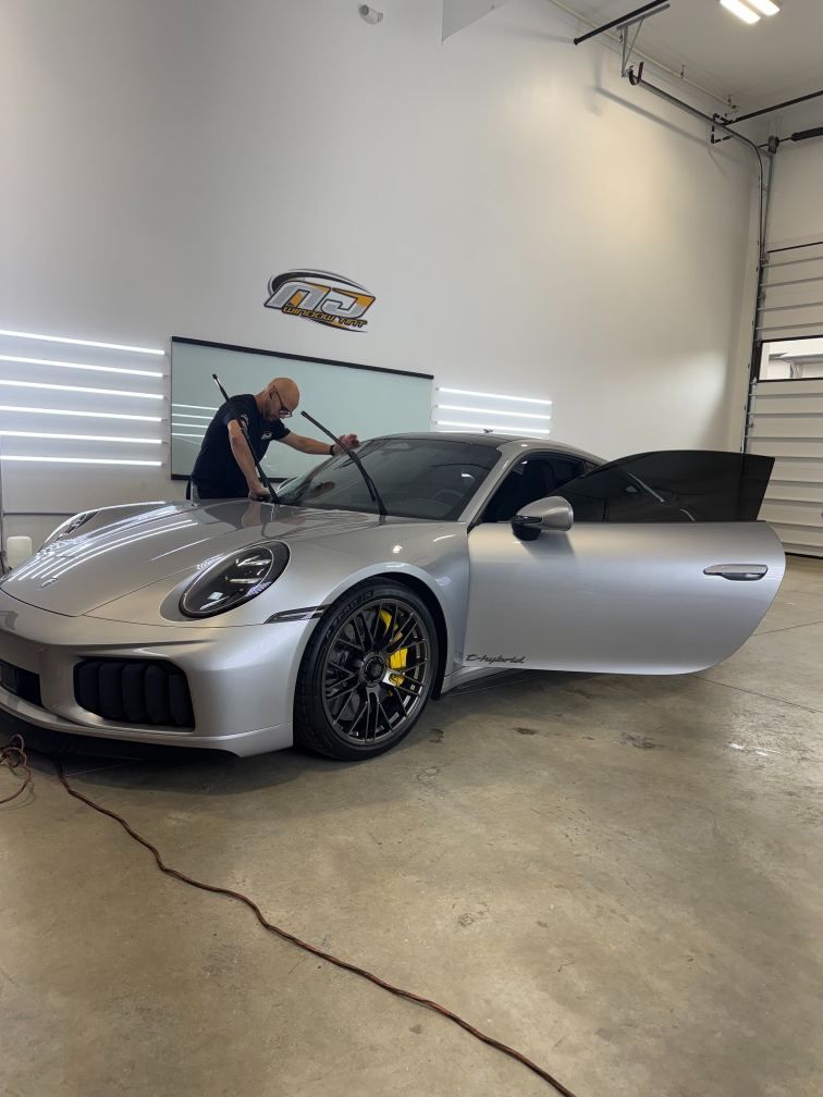 Silver Porsche 911 in a garage, front hood open, with a person cleaning the windshield.