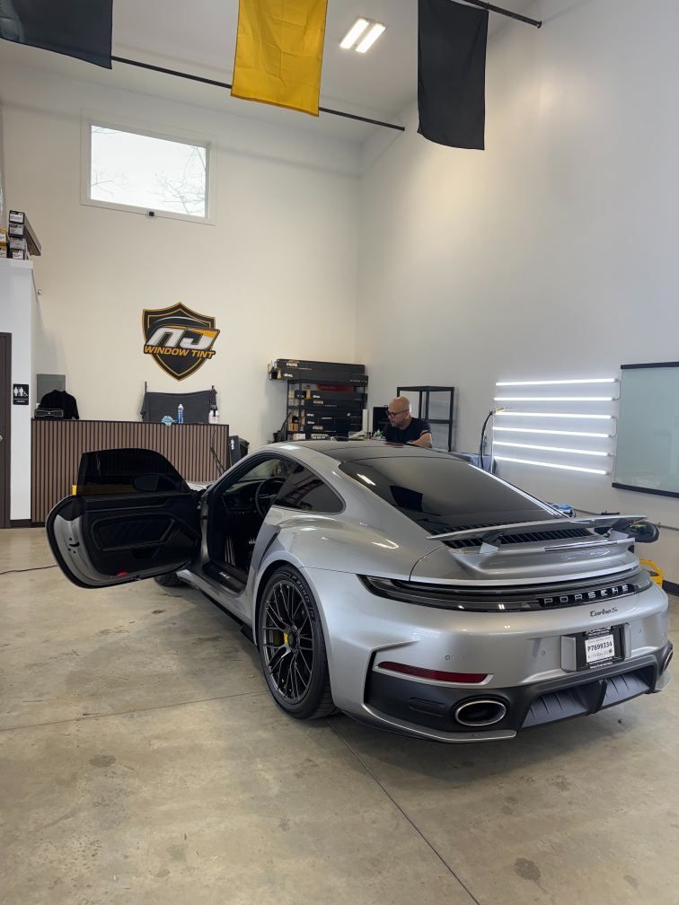 Silver sports car parked in a garage with the driver door open and rear engine cover lifted