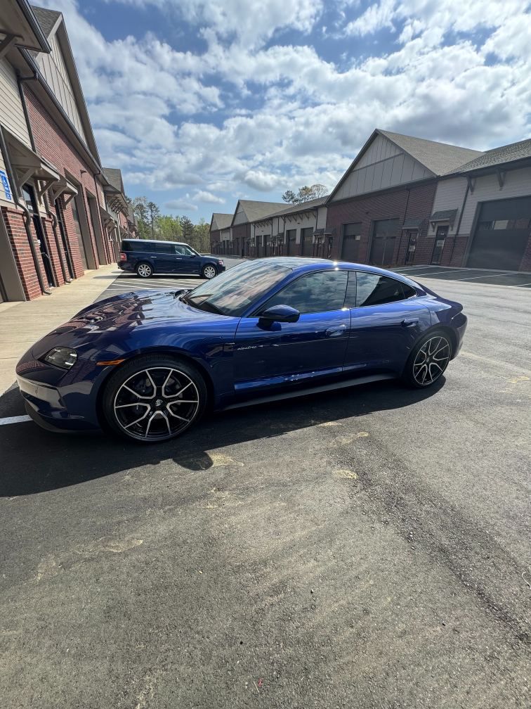 Blue sports coupe parked outside brick buildings on a sunny street.