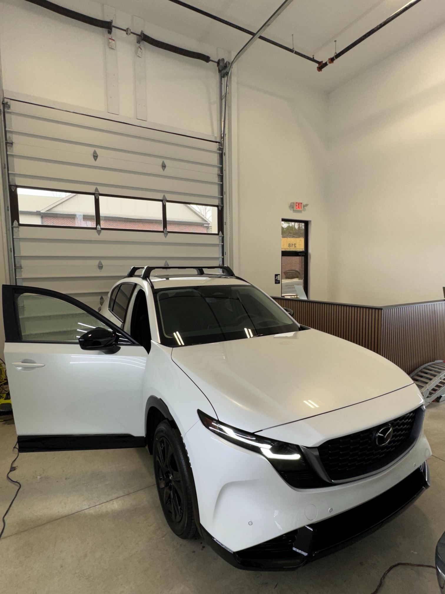 White SUV parked inside a garage, driver door open, with a high overhead door in the background