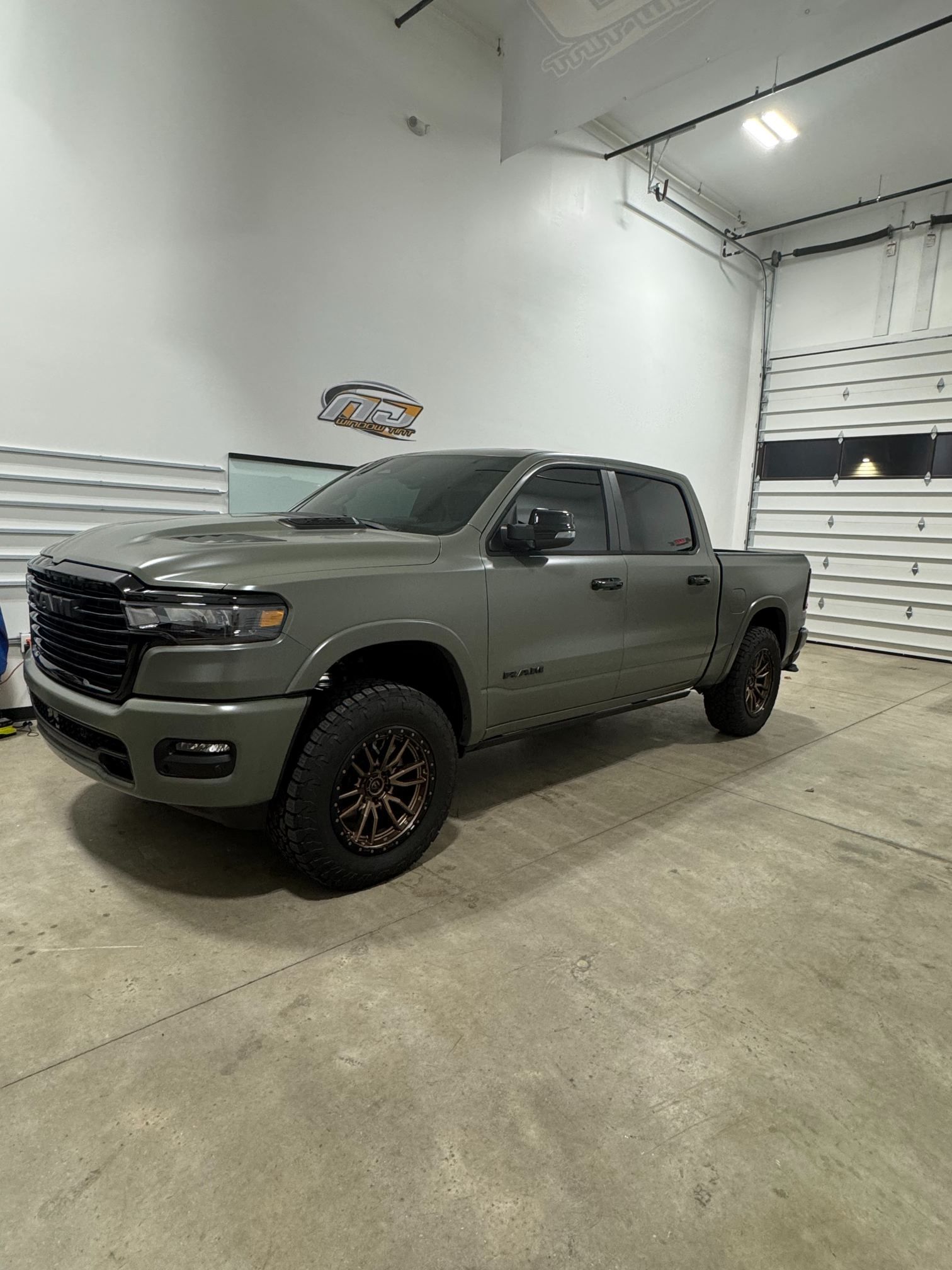 A black lifted pickup truck with custom wheels parked in front of a building with tire brand signage.