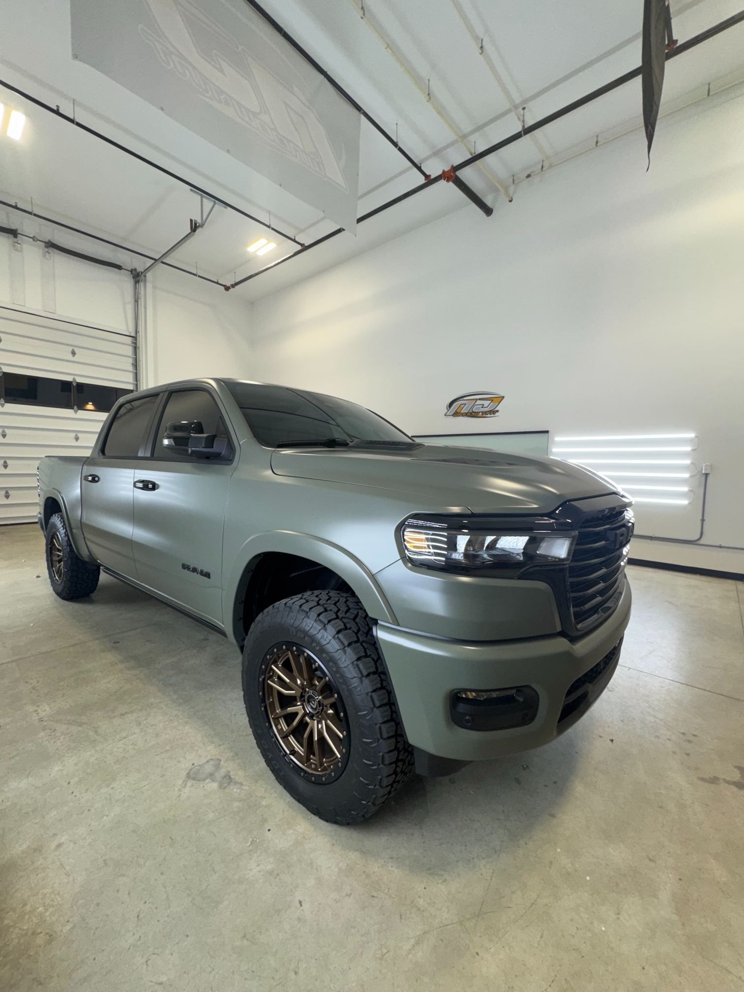Silver pickup truck in a garage, angled front view, with black grille and off-road tires.