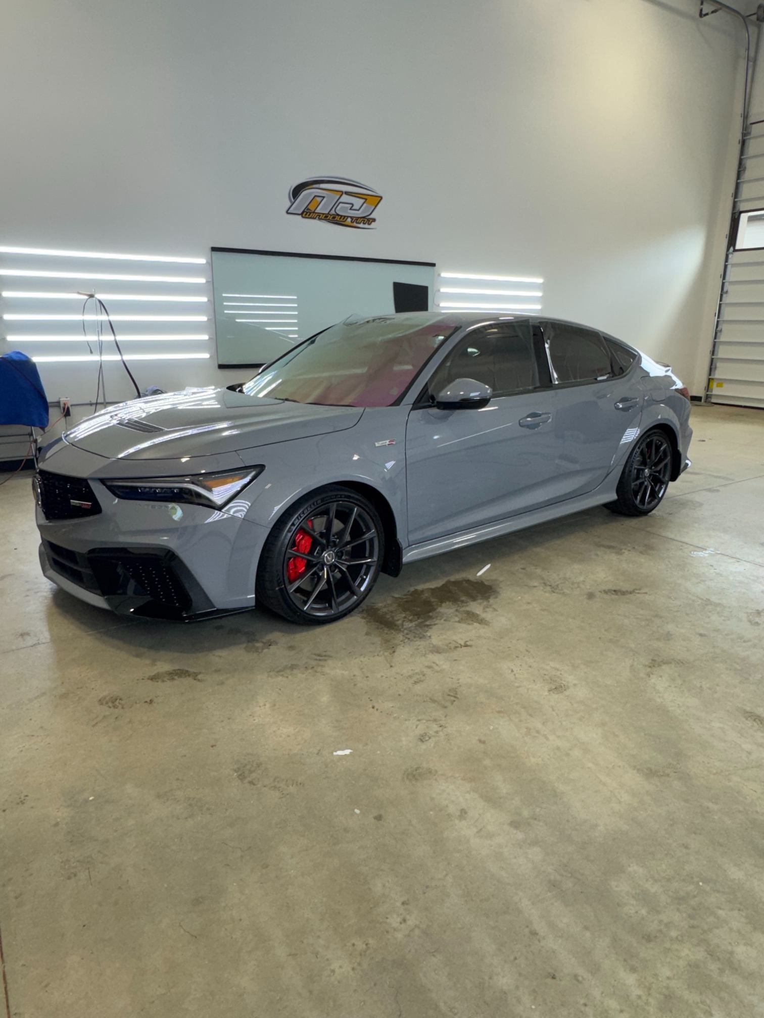 Gray sport sedan with black wheels and red brake calipers parked in a bright garage