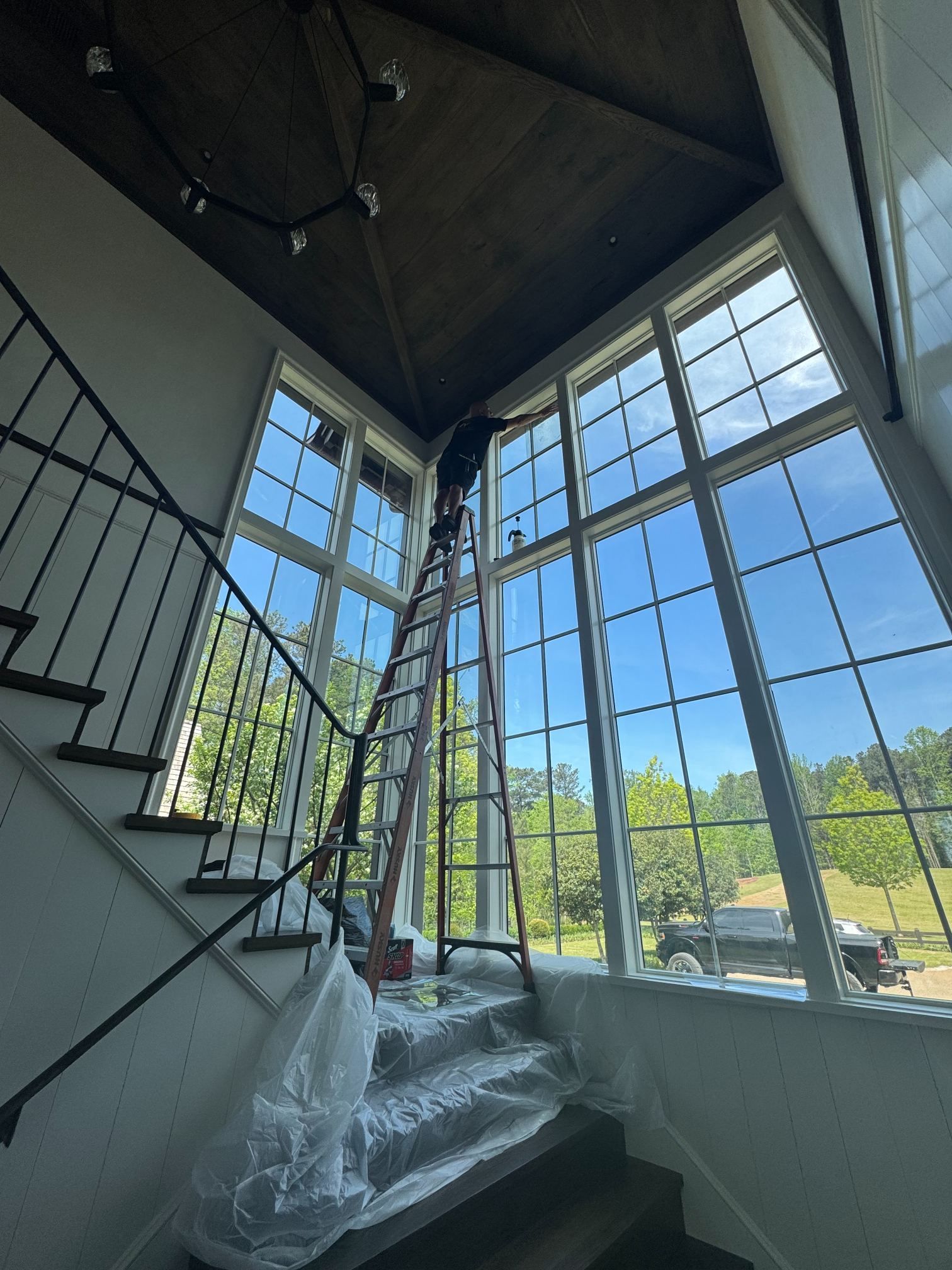 Modern staircase in a bright atrium with large floor-to-ceiling windows and protective plastic covering the steps
