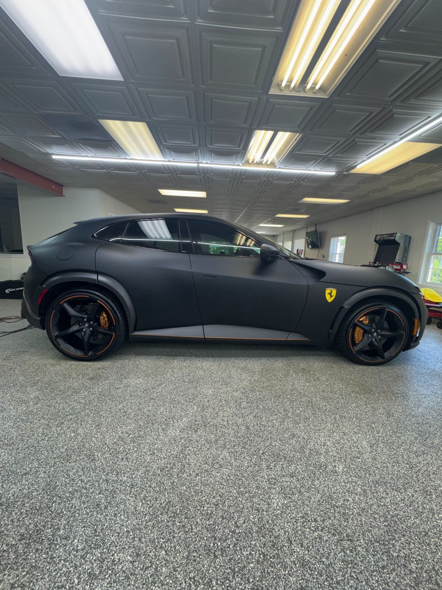Matte black sports coupe parked indoors under bright ceiling lights