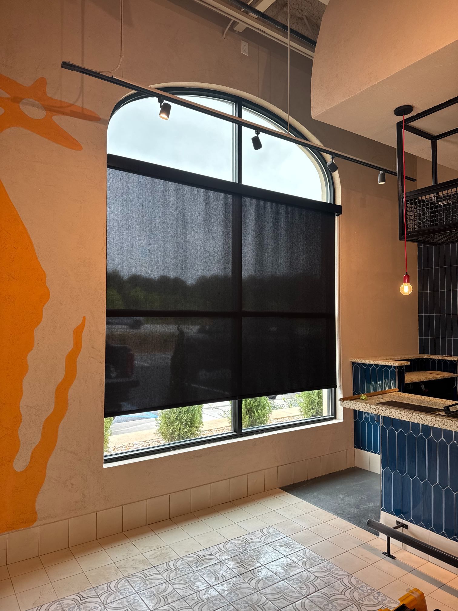 Interior with arched window covered by black blinds, orange walls, and blue cabinetry in a kitchen.
