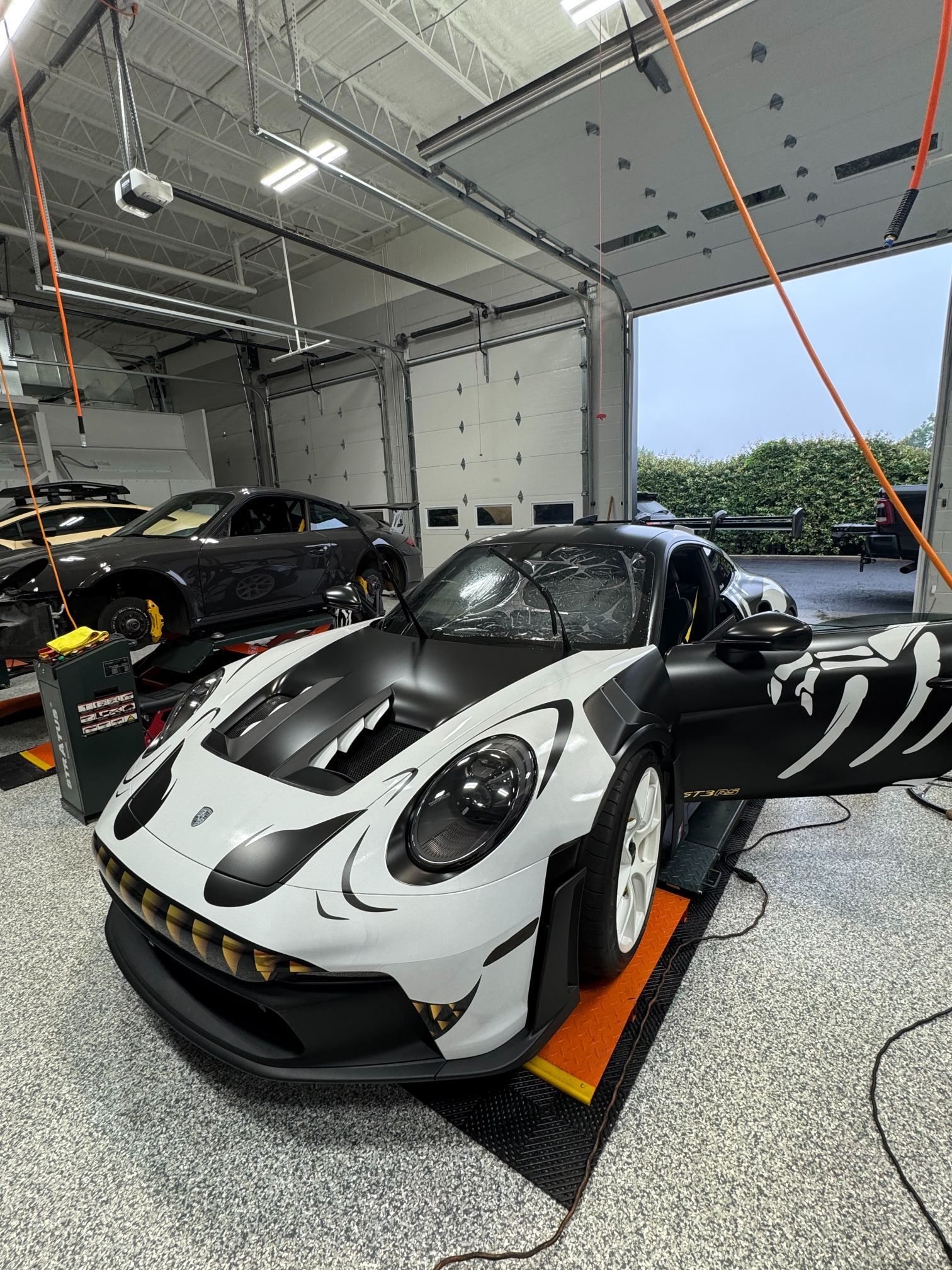 White-and-black sports car in a garage, with two other cars parked nearby.