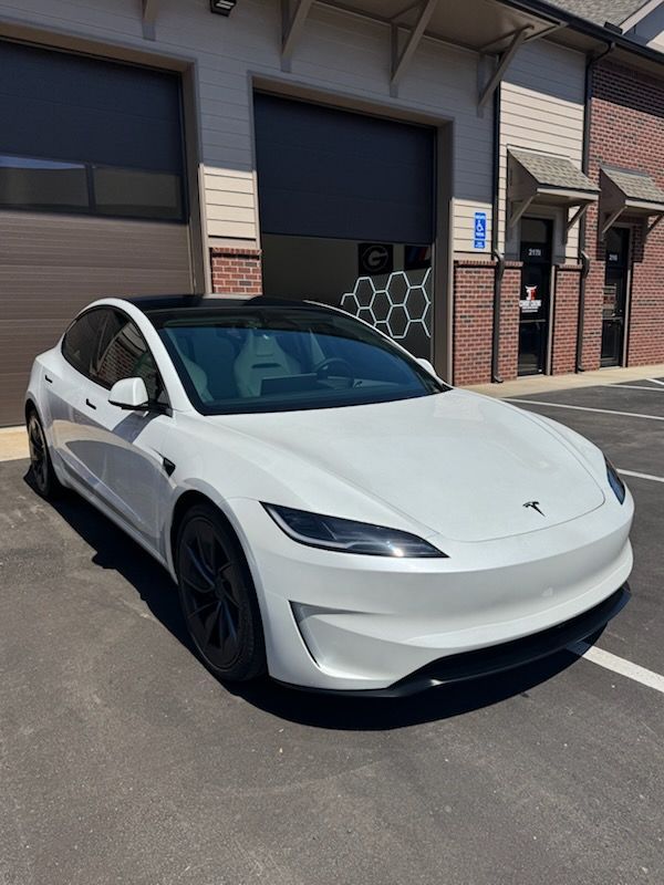 White Tesla parked on a sunny street in front of garage doors and brick buildings