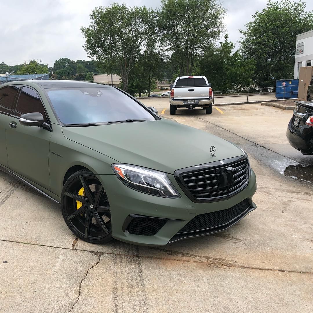 A matte olive green Mercedes-Benz sedan with black wheels and yellow brake calipers parked in a paved lot.