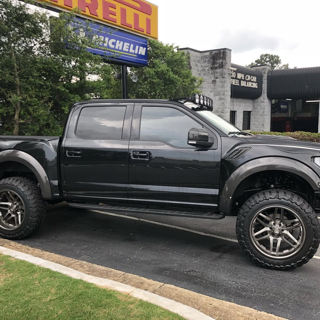 A black lifted pickup truck with custom wheels and a roof-mounted light bar parked in front of an automotive shop.