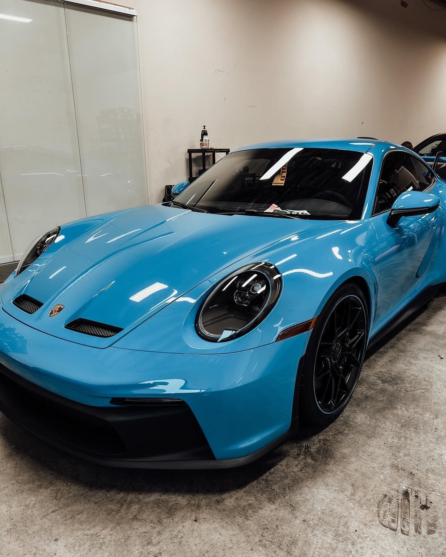 A vibrant blue Porsche 911 GT3 parked in a bright, minimalist indoor showroom with concrete floors.