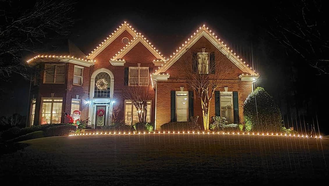 A large brick house is decorated with christmas lights at night.