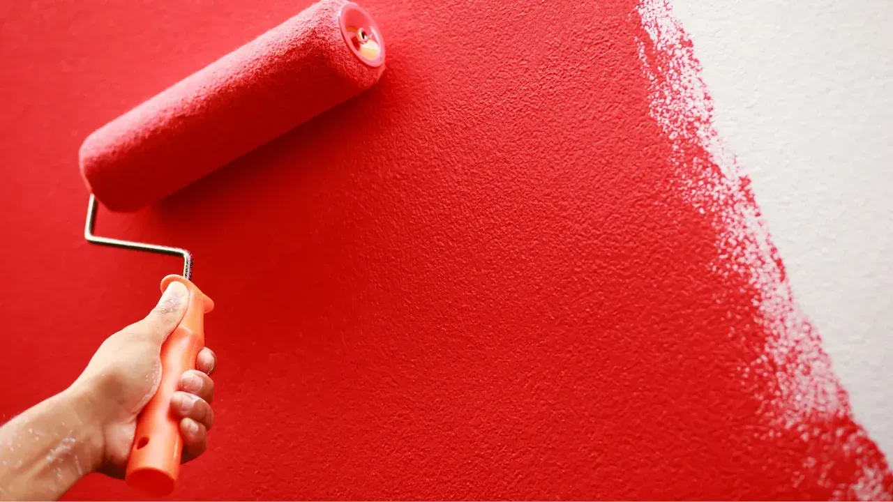 A red paint roller painting on a white wall