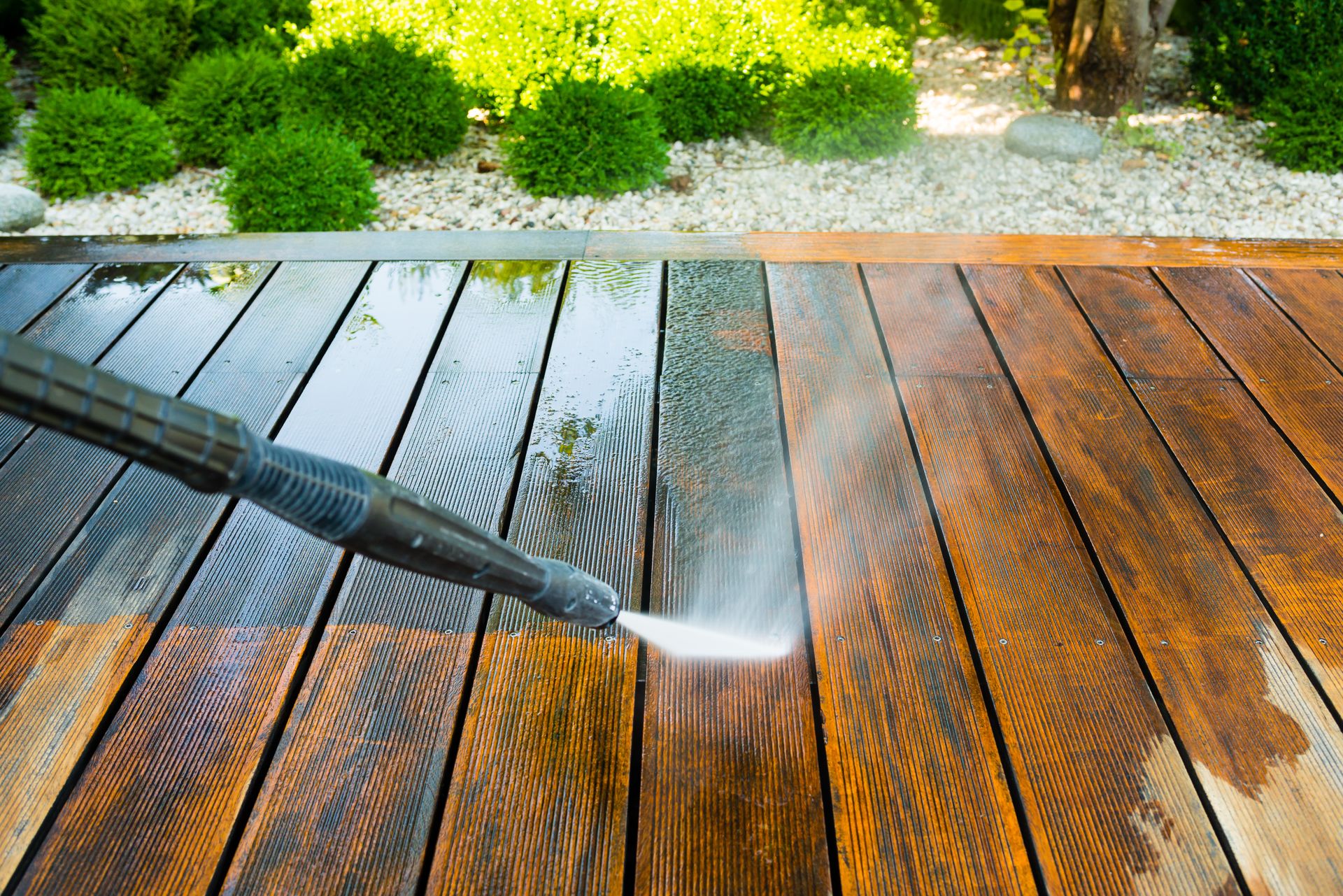 A pressure washer cleans grime off wooden deck planks, showing a clear contrast between dirty and clean areas.