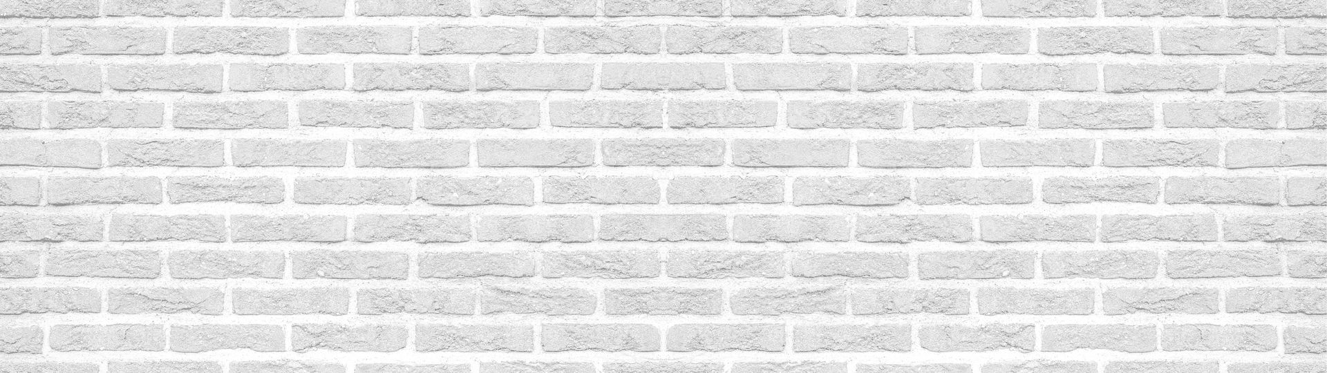 A worker in a blue shirt and green cap uses a power washer to clean a dark brick wall.