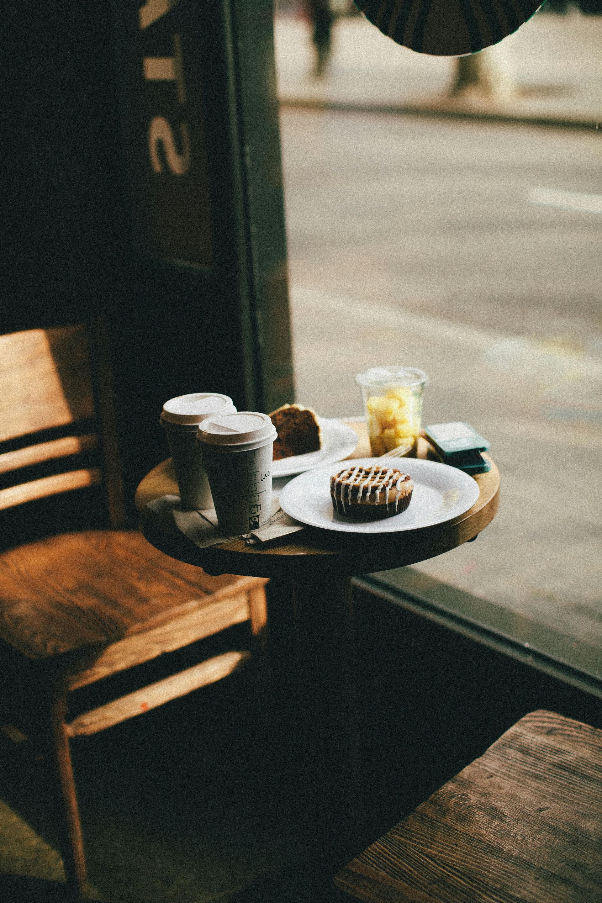 A table with plates of food and drinks on it in front of a window.