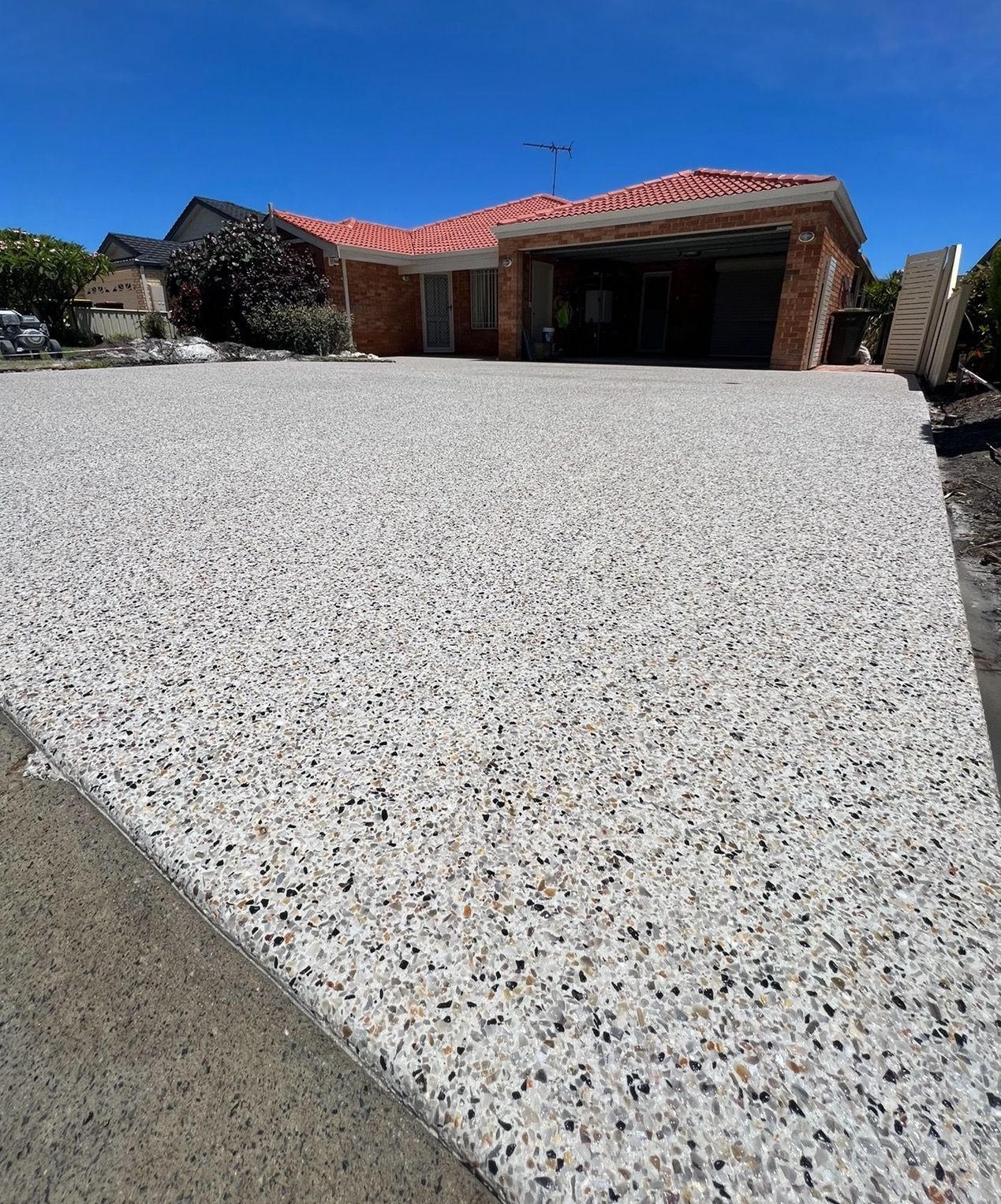 Wide driveway leading to a single-story house with a red tile roof under a clear blue sky.